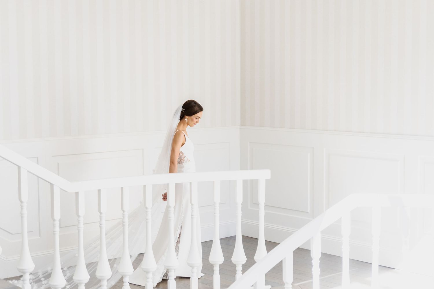 A person in a white dress walks down an elegant white staircase in a bright minimalist interior.