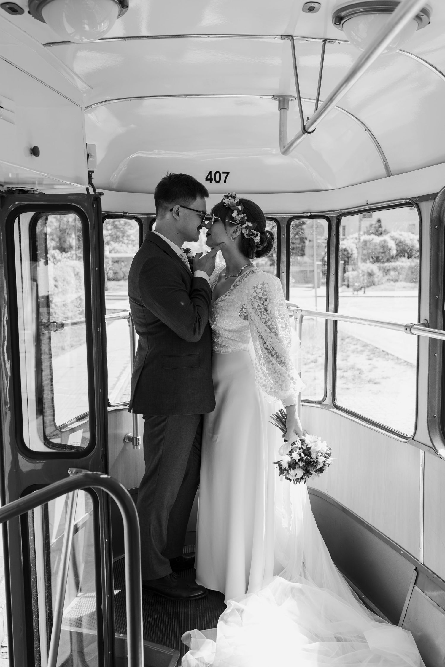 A romantic black and white wedding photo captures a tender moment inside vintage bus number 407.