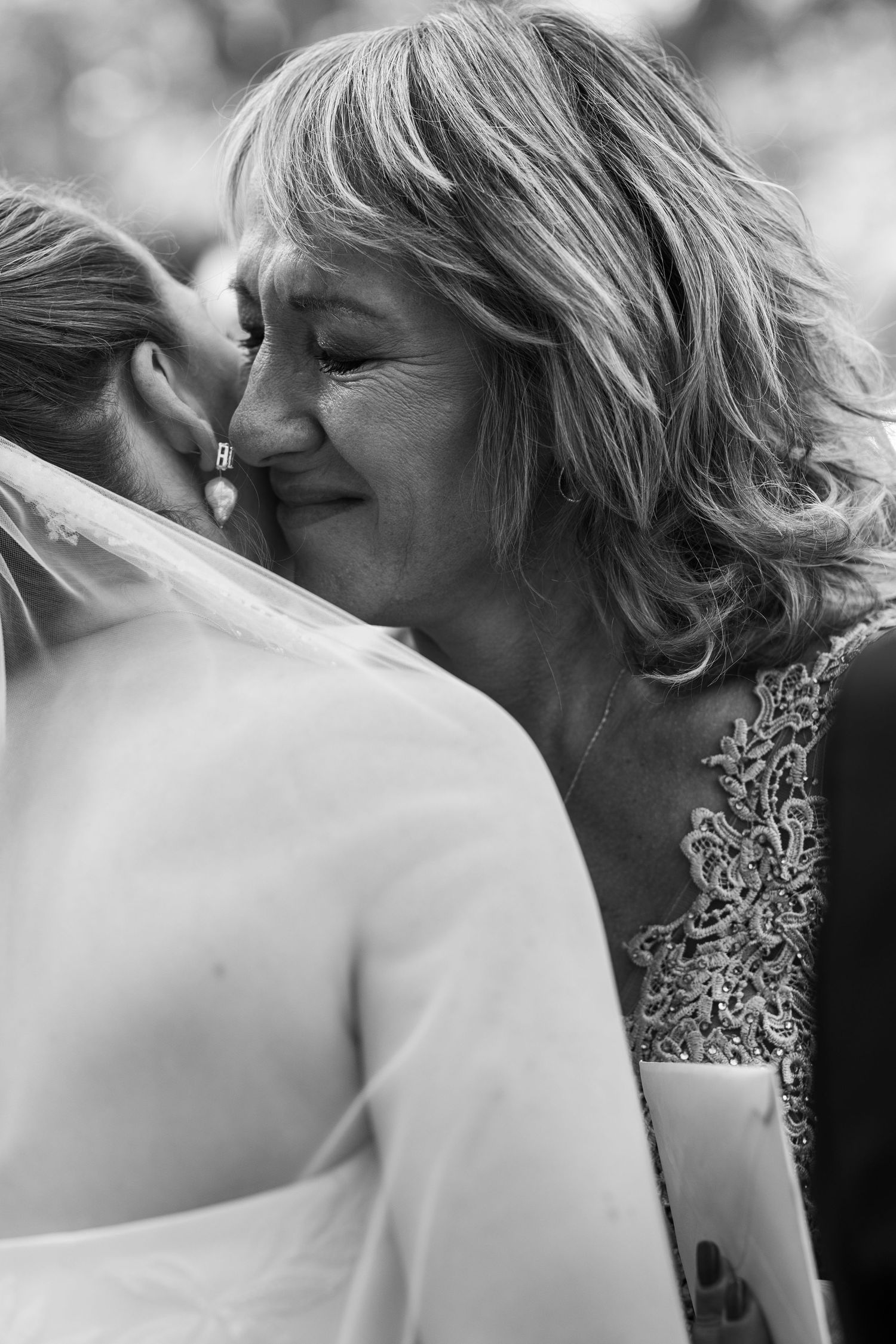 Black and white intimate moment showing emotional embrace at wedding with lace dress detail.