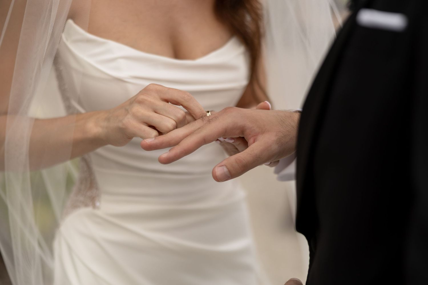 Bride and groom exchanging wedding rings during ceremony, close-up of hands with diamond engagement ring.