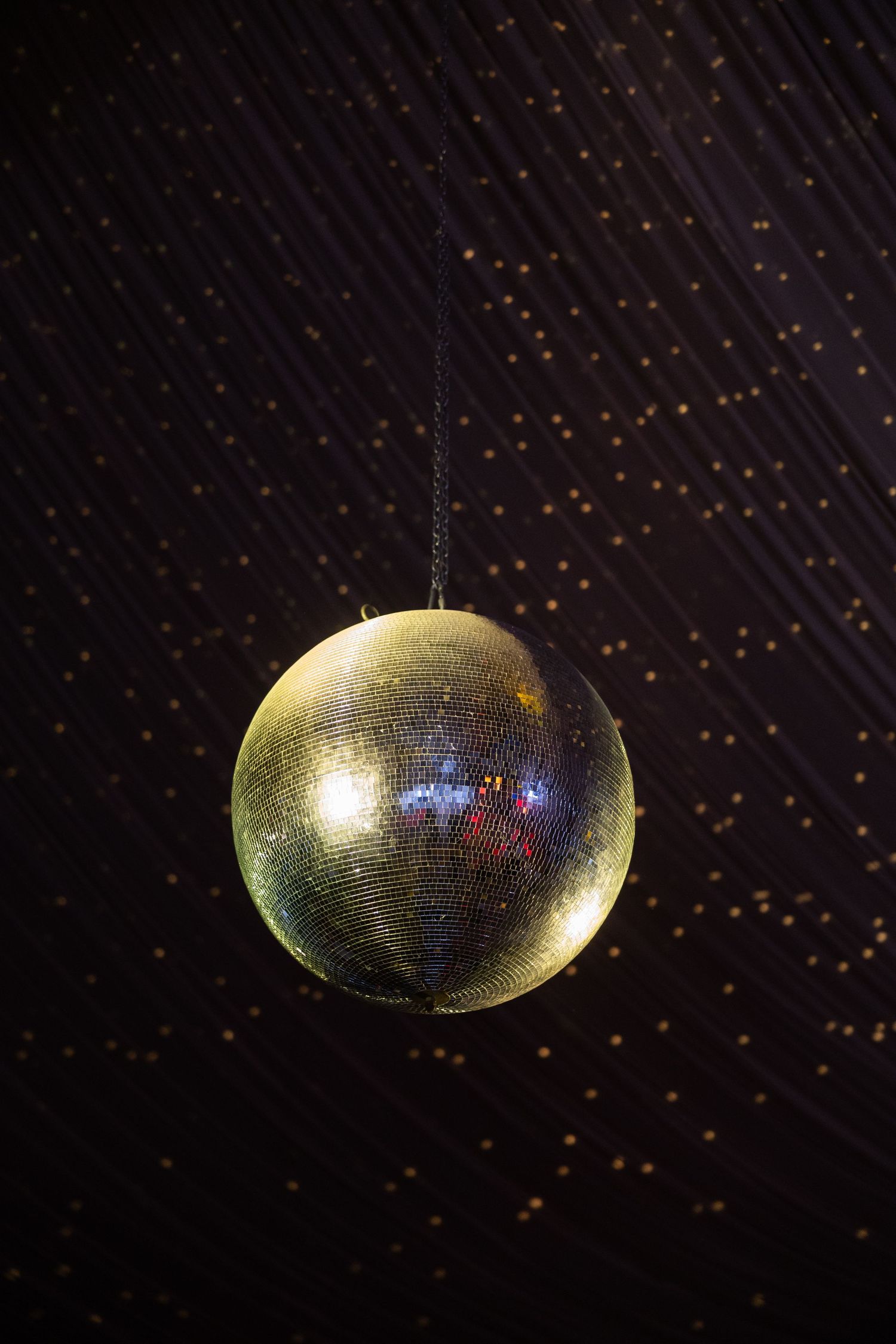 A shimmering gold disco mirror ball hanging from a dark ceiling with sparkling light reflections.