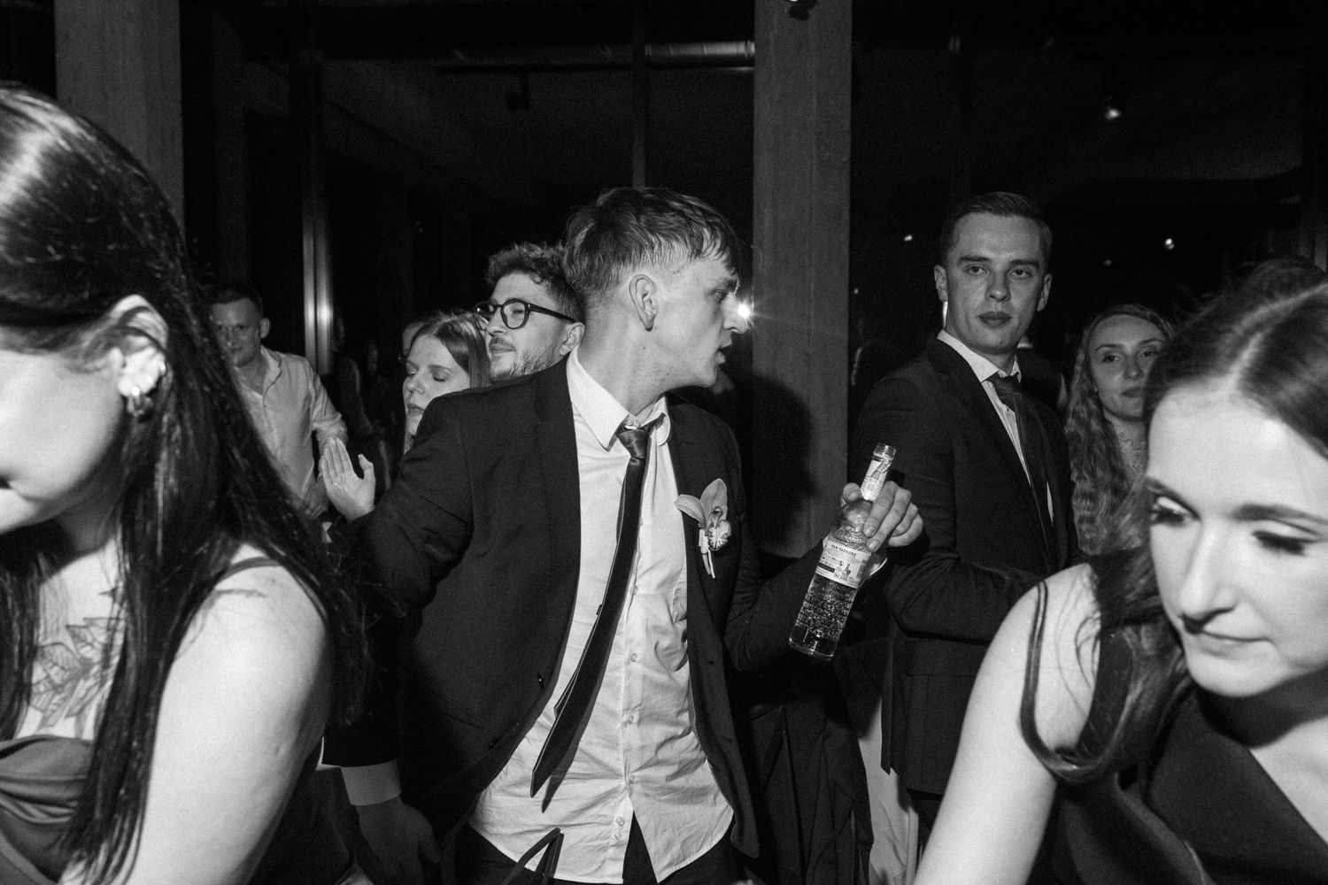 Black and white photo of people dancing and socializing at a party with formal attire and drinks.