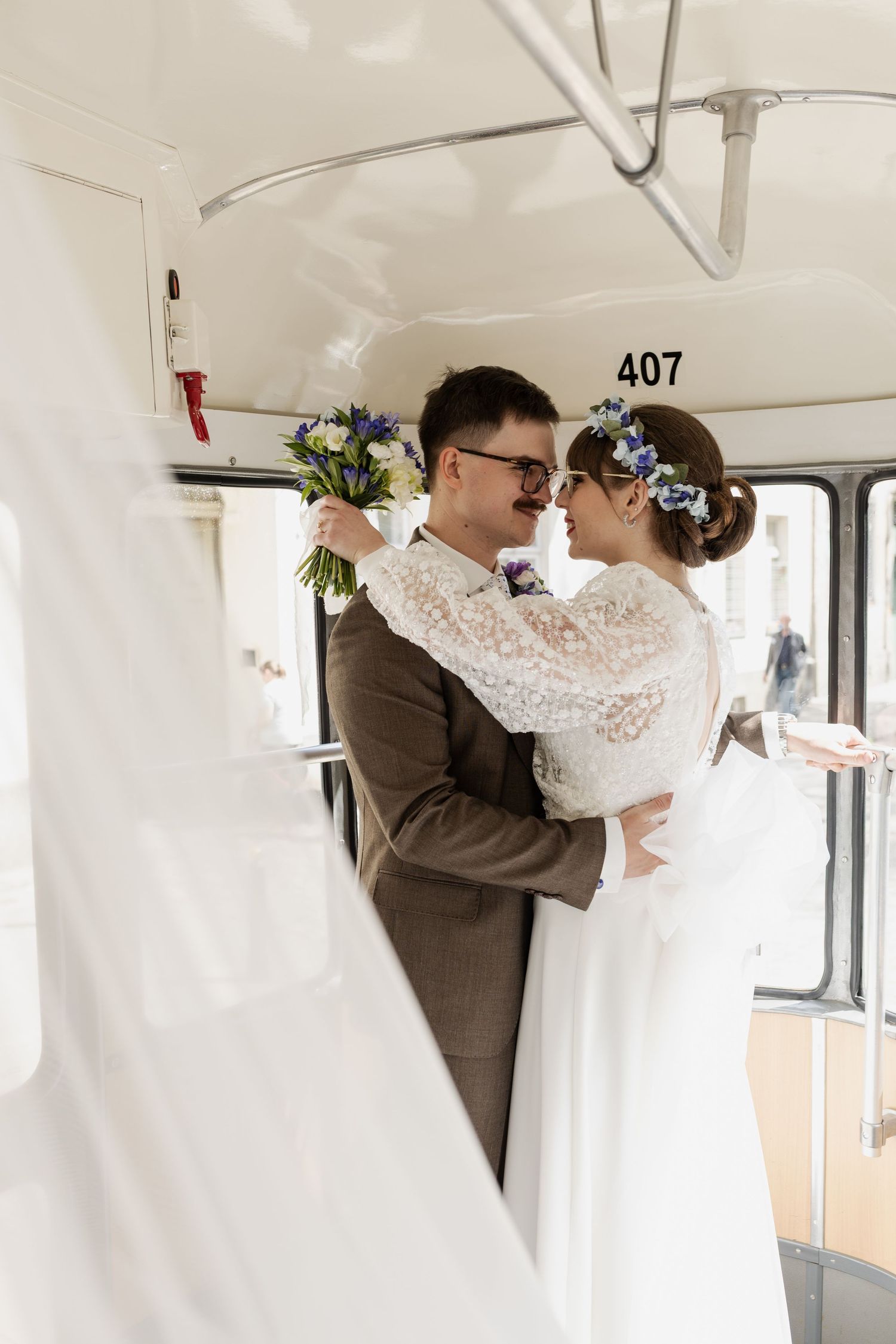 Newly married couple sharing an intimate moment inside vintage bus number 407 with bride holding blue flower bouquet.