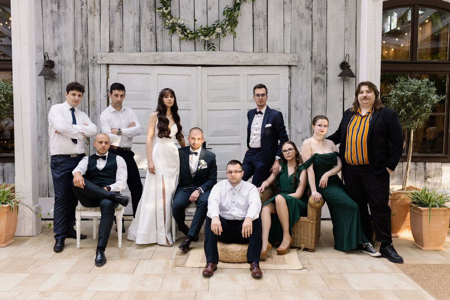 A stylish wedding party in formal black, white and green attire poses together in front of a rustic barn door.
