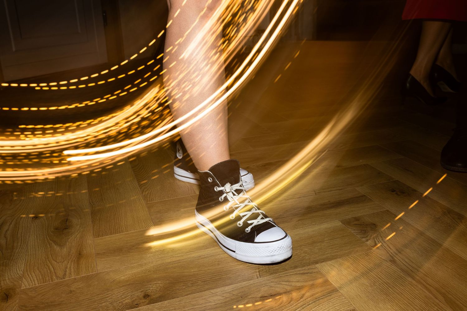 Long exposure photograph of light trails swirling around a black Converse sneaker on a wooden floor.