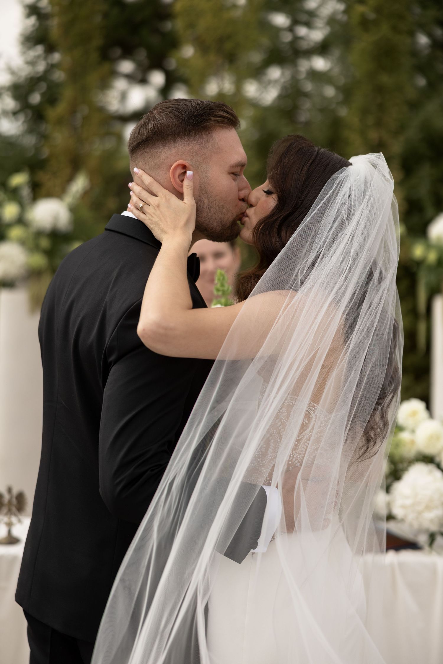 Bride and groom sharing their first kiss at outdoor wedding ceremony, bride wearing white veil and lace dress.