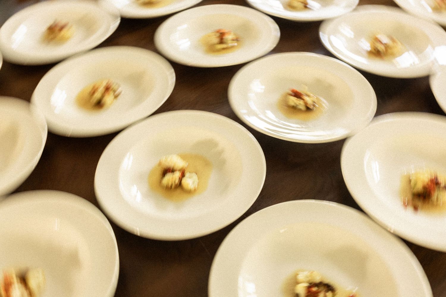 Overhead view of multiple oysters topped with garnish and served on white plates arranged in neat rows.