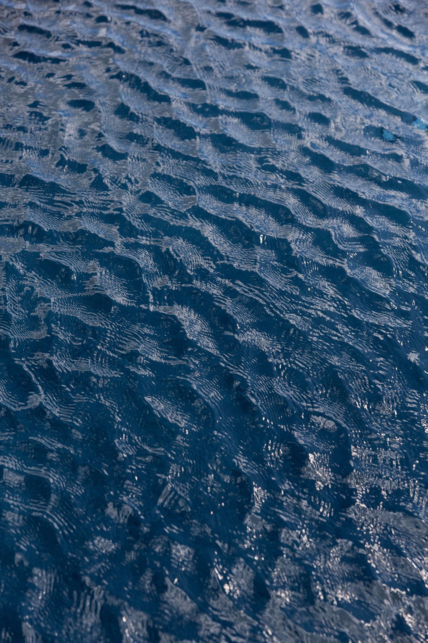 Close-up aerial view of dark blue rippling water surface with gentle wave patterns creating a textured abstract background.