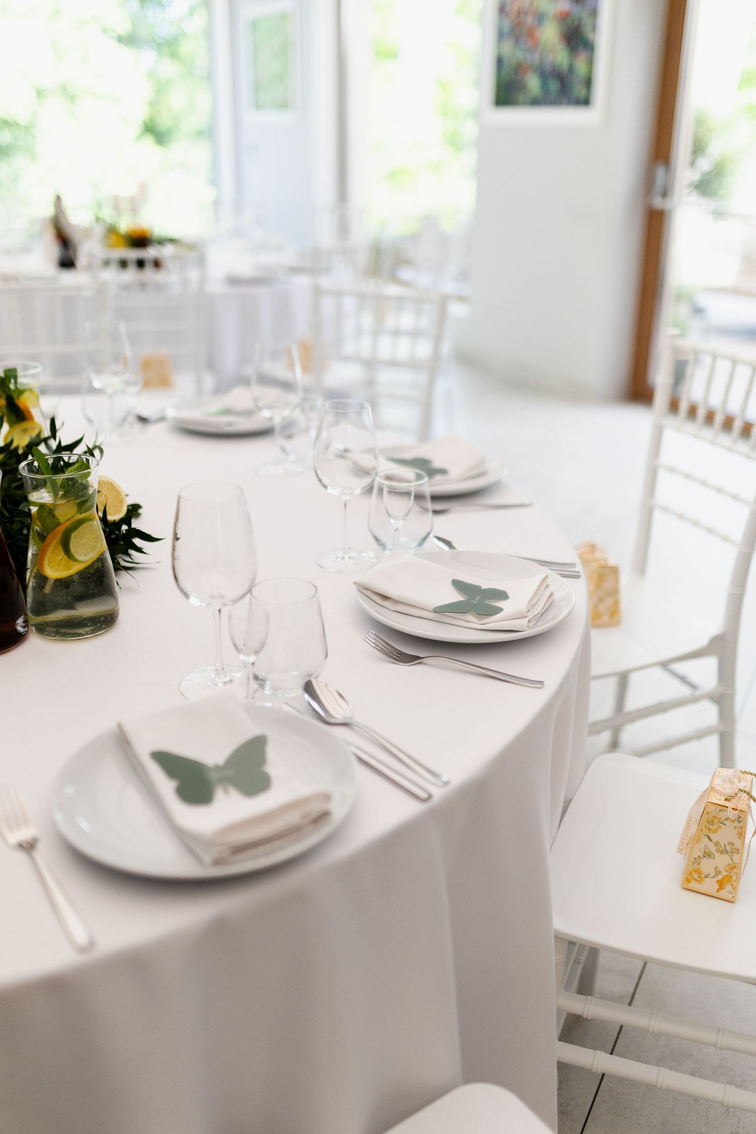 Elegant table setting with white linens, butterfly place cards, wine glasses and white chiavari chairs at a wedding reception.
