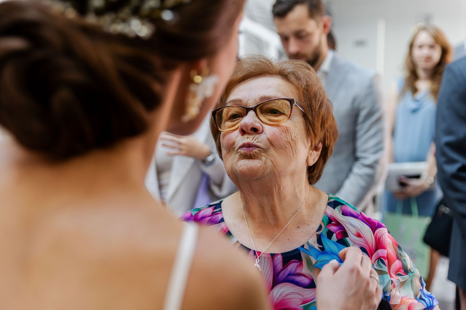 A person in glasses wearing a vibrant purple patterned top smiles warmly during a social gathering.