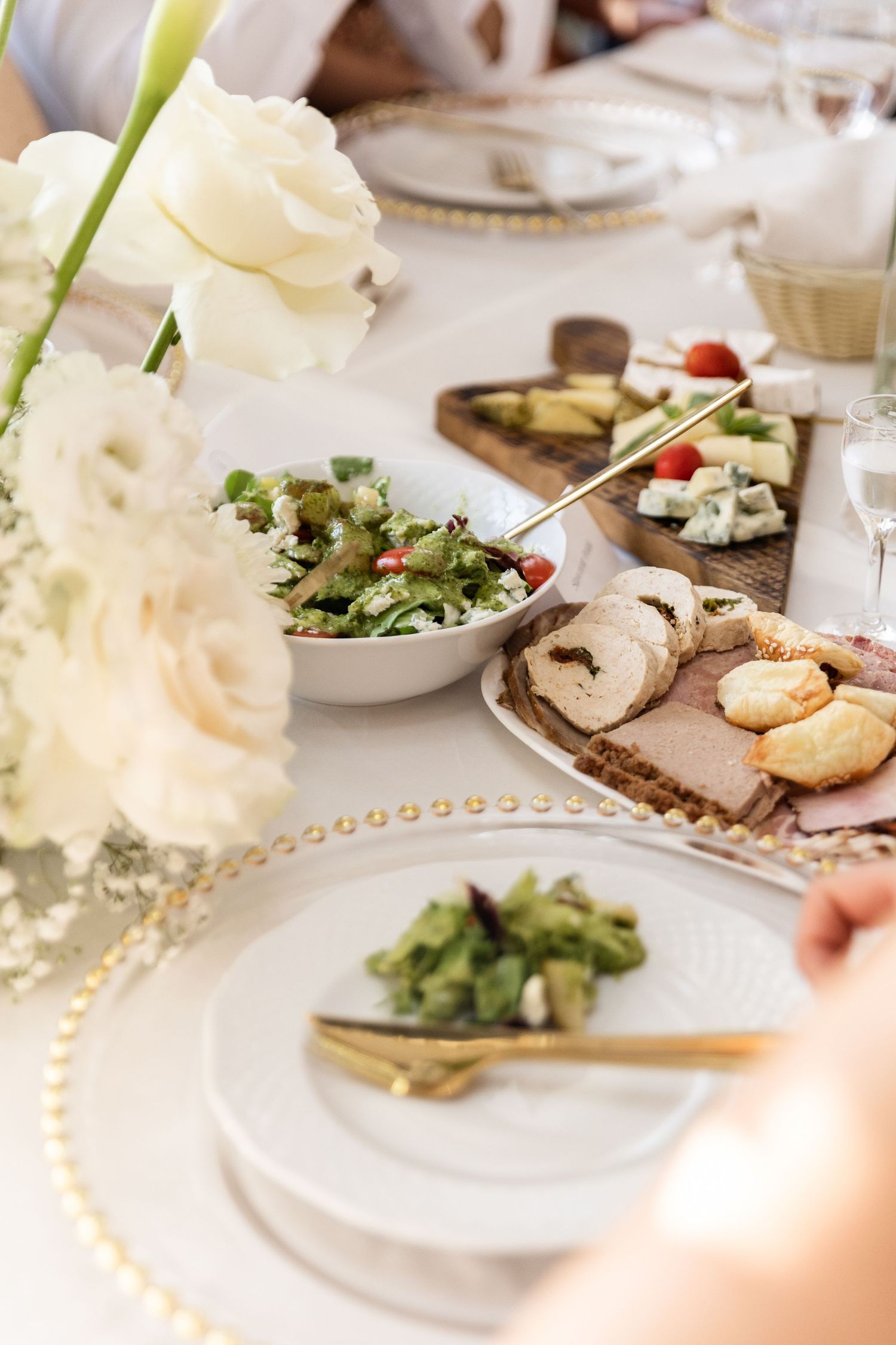 Elegant place settings with white plates, fresh salads, and bread arranged on a dining table with white floral centerpieces.