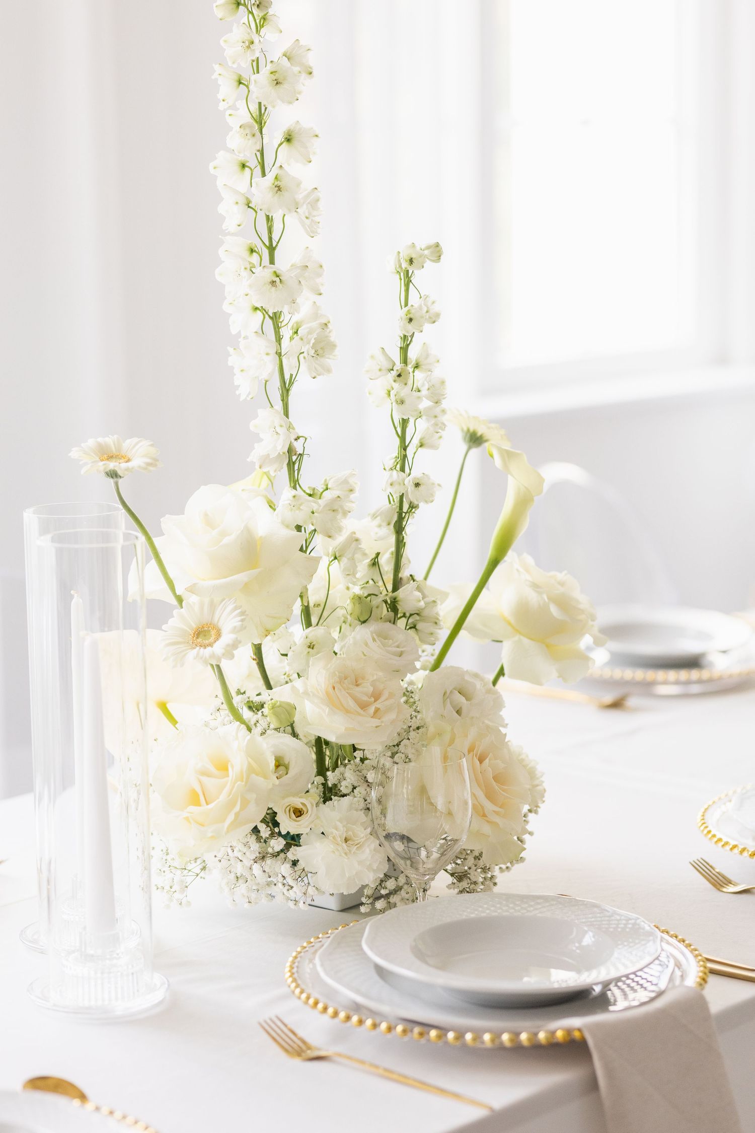 Elegant white table setting with delicate floral arrangements of roses and baby's breath in crystal vases.