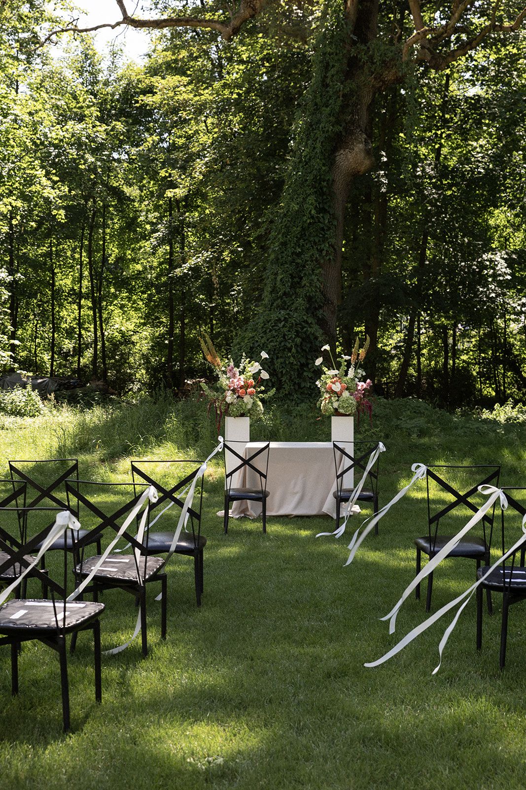 Rows of black metal chairs arranged outdoors on grass with white fabric covers and pink floral decorations.