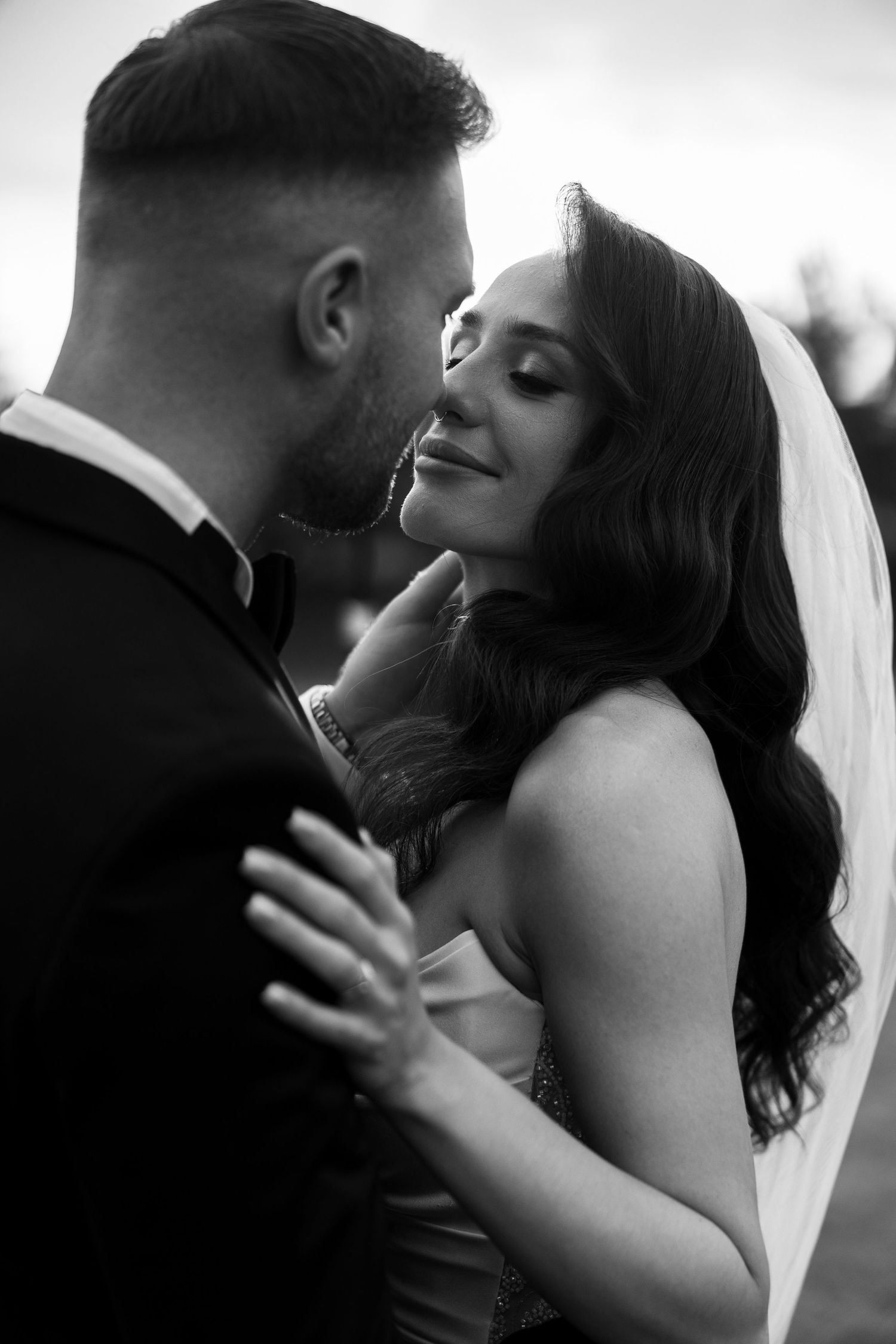 Black and white wedding photo of bride and groom sharing an intimate moment, bride smiling softly in veil and gown.