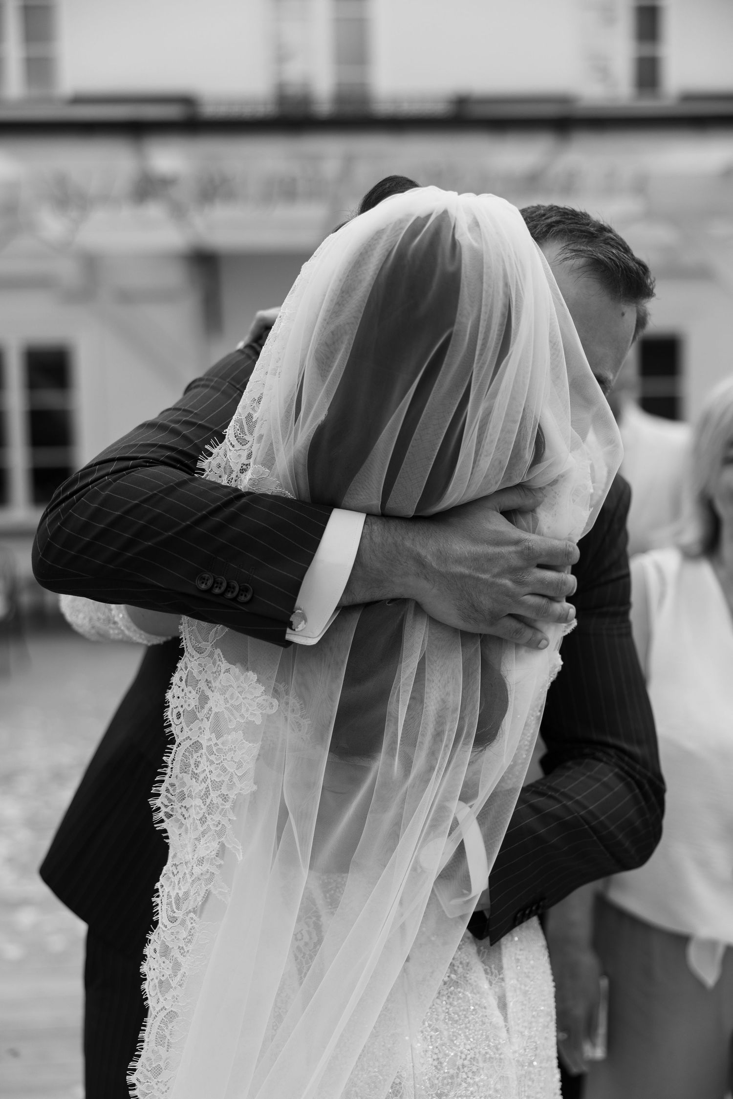 Black and white photo of bride and groom embracing, bride wearing lace wedding dress and veil.