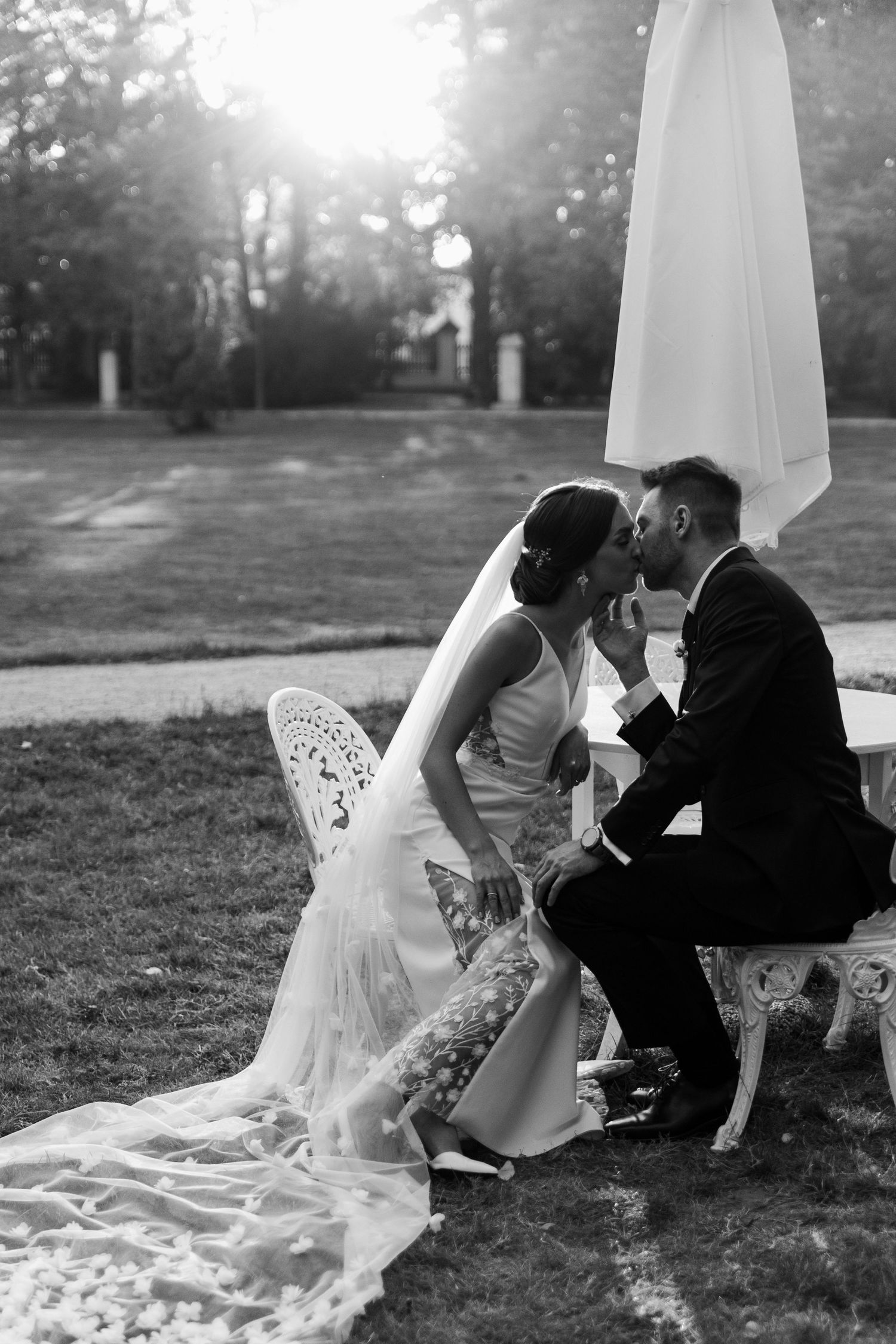 Black and white romantic wedding photo showing a couple sharing an intimate moment on an ornate outdoor bench.
