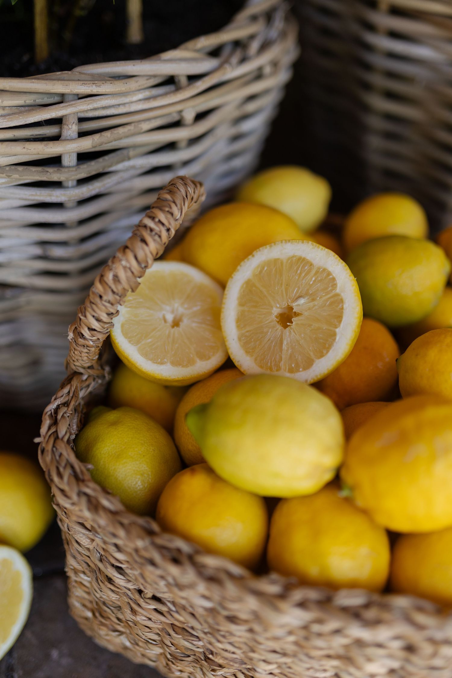 Fresh yellow lemons displayed in a rustic woven basket with two halves showing juicy flesh and pith.