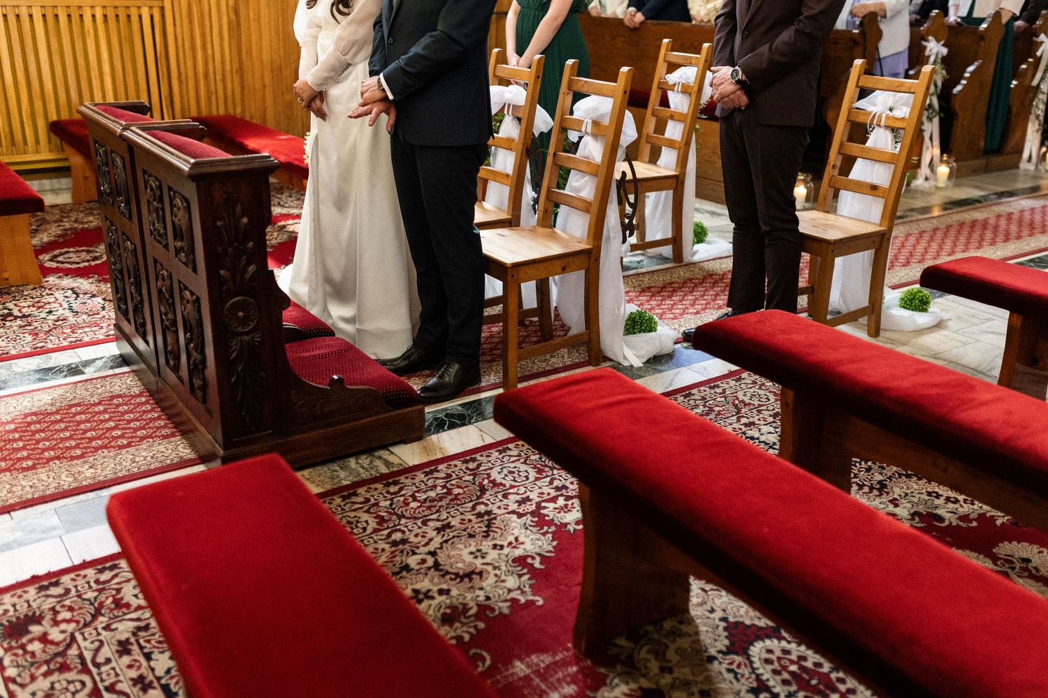 Red prayer cushions and ornate carpets arranged at the altar during a wedding ceremony in a church.