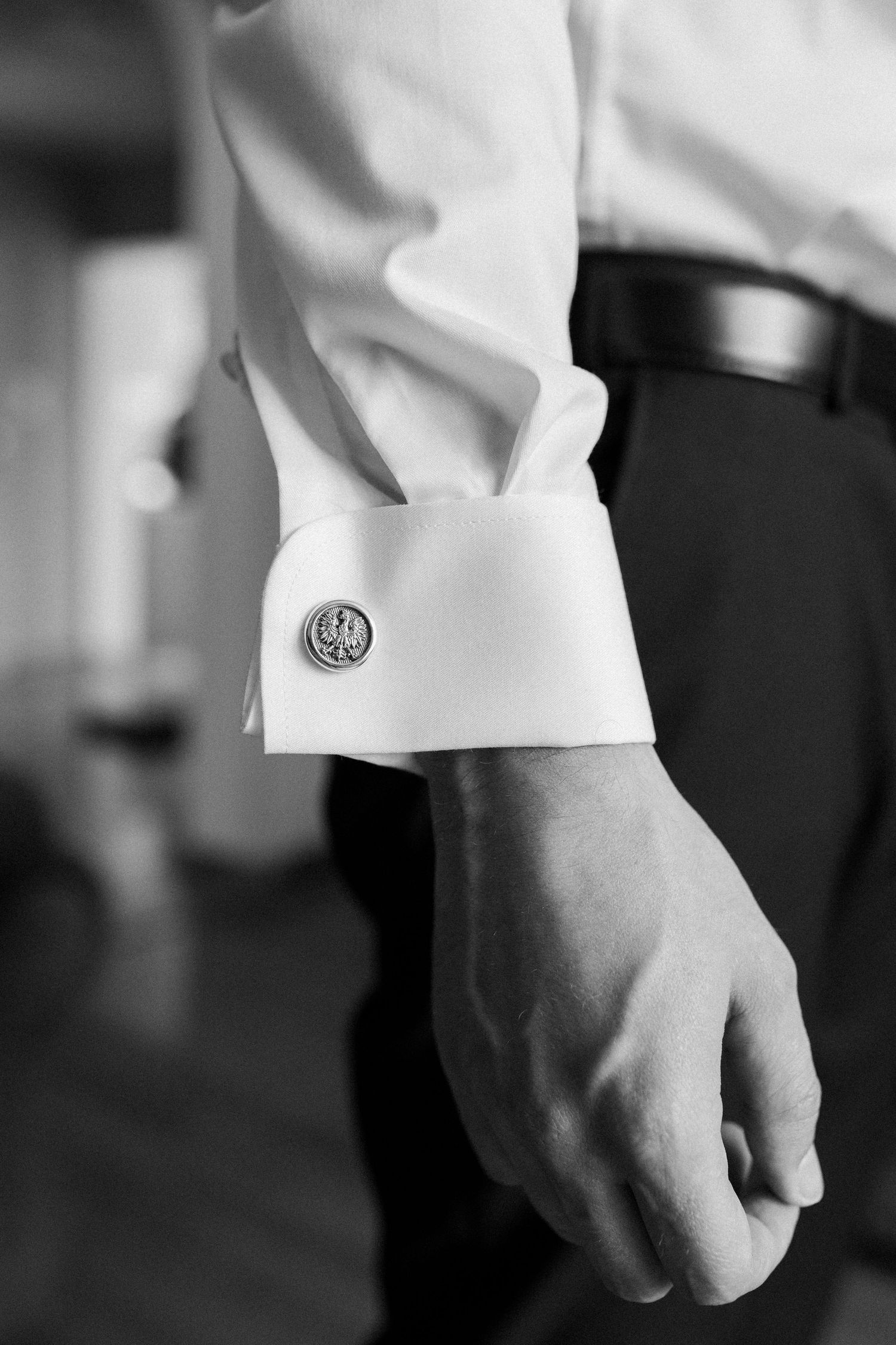 A close-up black and white photo of a white dress shirt cuff with a decorative cufflink detail.