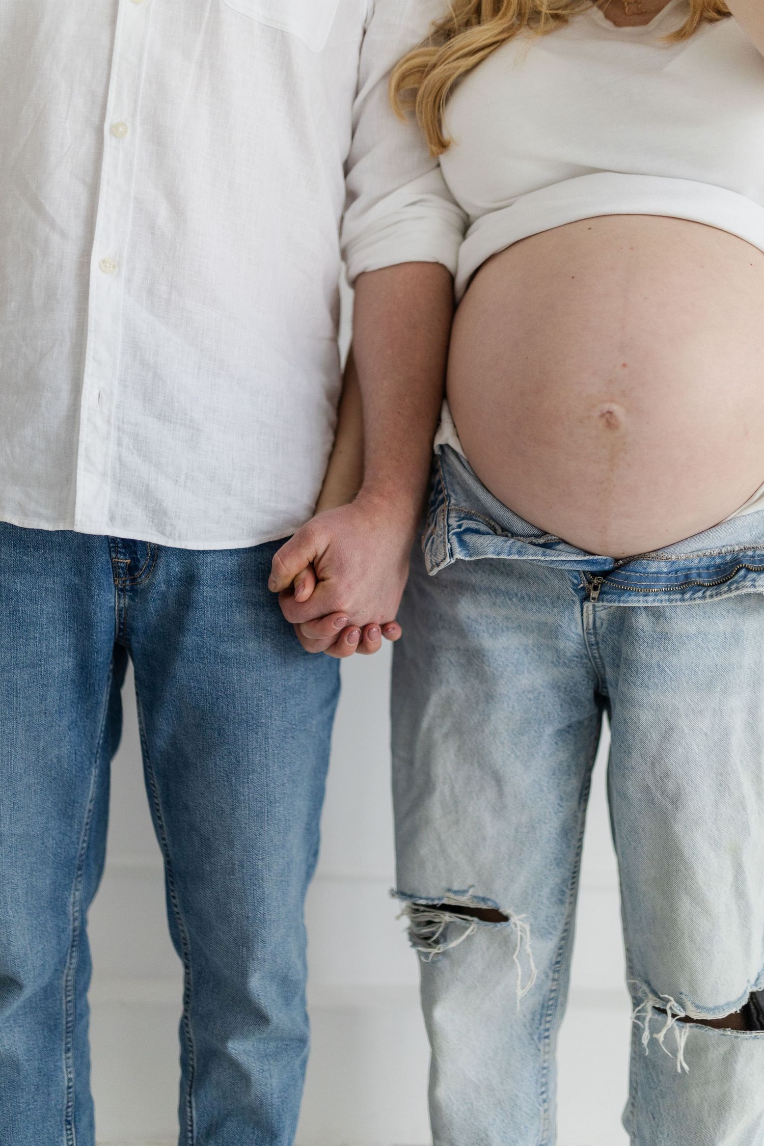 Close-up of expecting couple holding hands, showing pregnant belly and wearing casual denim jeans.