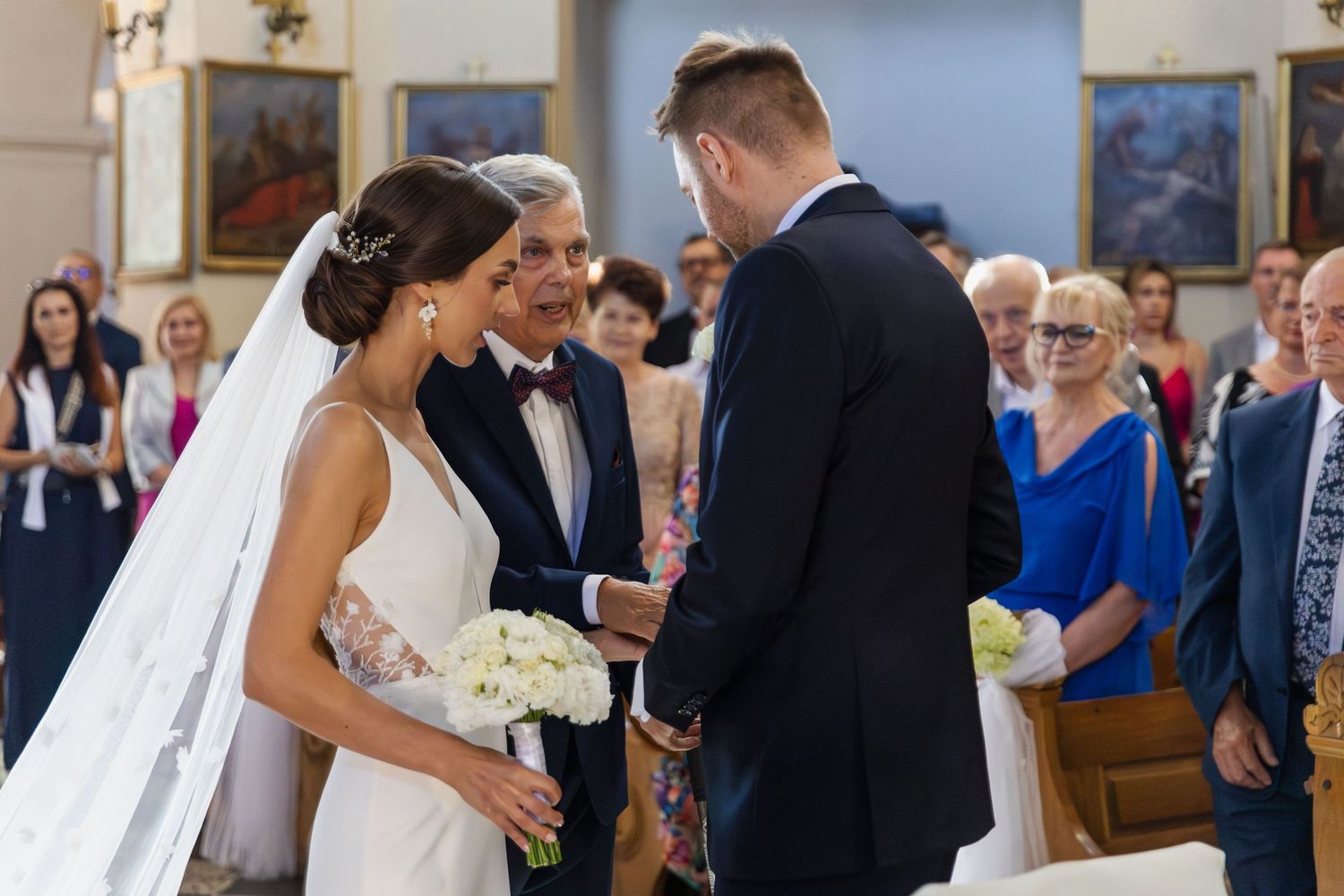 A couple exchanges rings during their wedding ceremony in a church while guests look on from the pews.