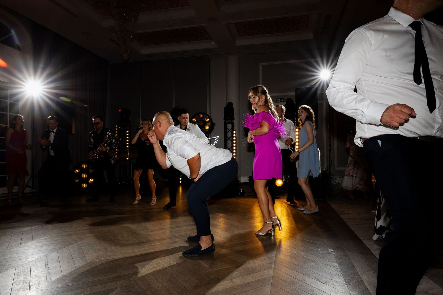 Wedding guests dancing and celebrating on a dark dance floor with camera flashes illuminating the lively party scene.