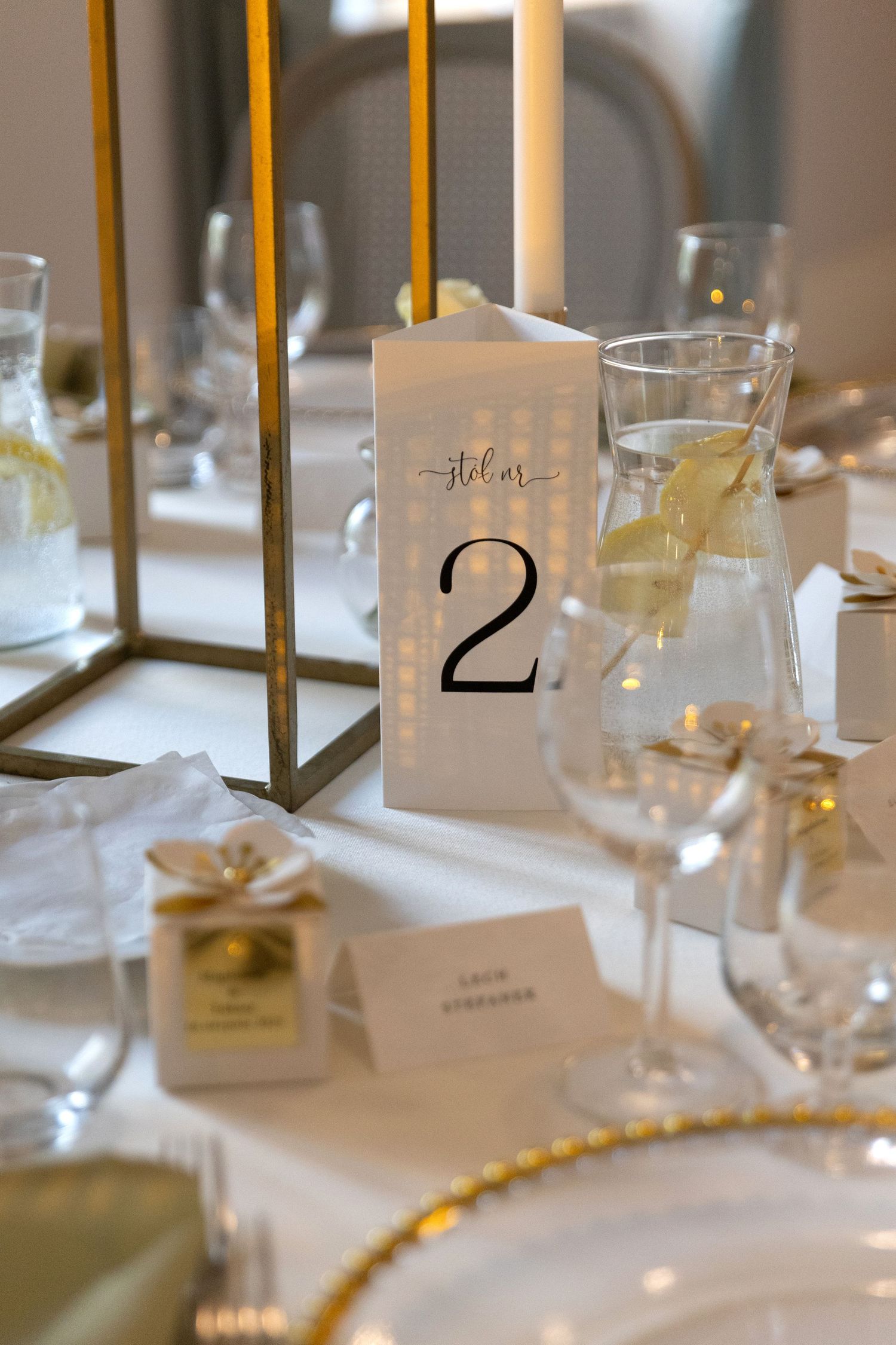 Elegant table setting with gold candle holders, white linens, and numbered table cards for a formal event.