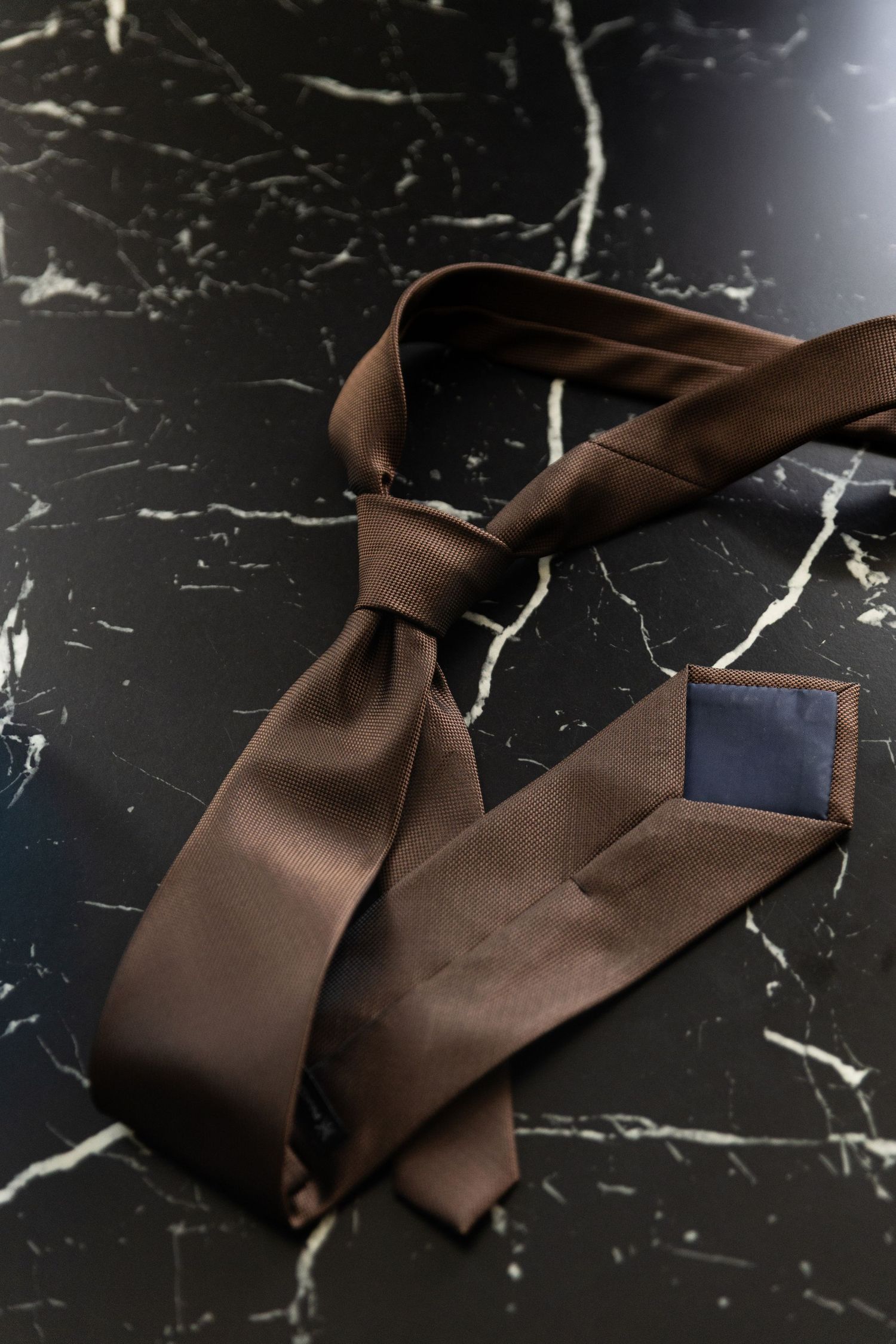 Brown silk ribbon lies gracefully twisted on a black marble surface creating an elegant composition.