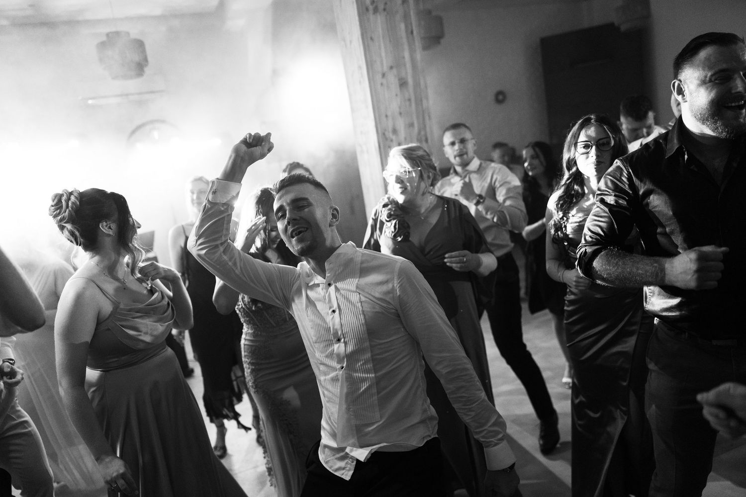 Black and white photo of guests dancing energetically at a wedding reception in an elegant ballroom.