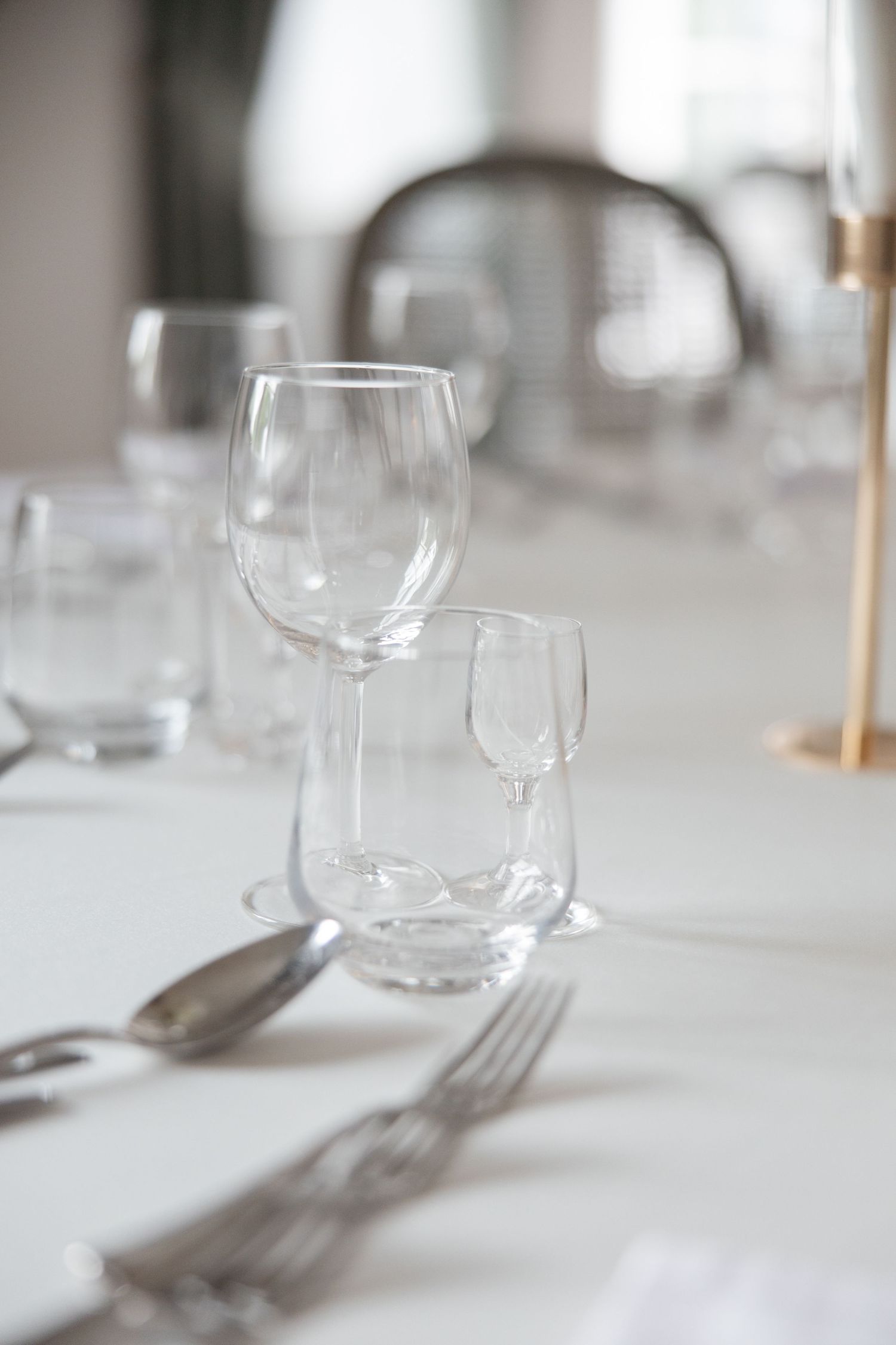 Elegant table setting with empty wine glasses, silverware, and white tablecloth in a formal dining room.