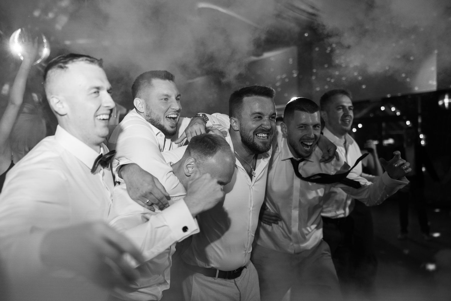 Black and white photo of groomsmen celebrating and dancing together at a wedding reception.