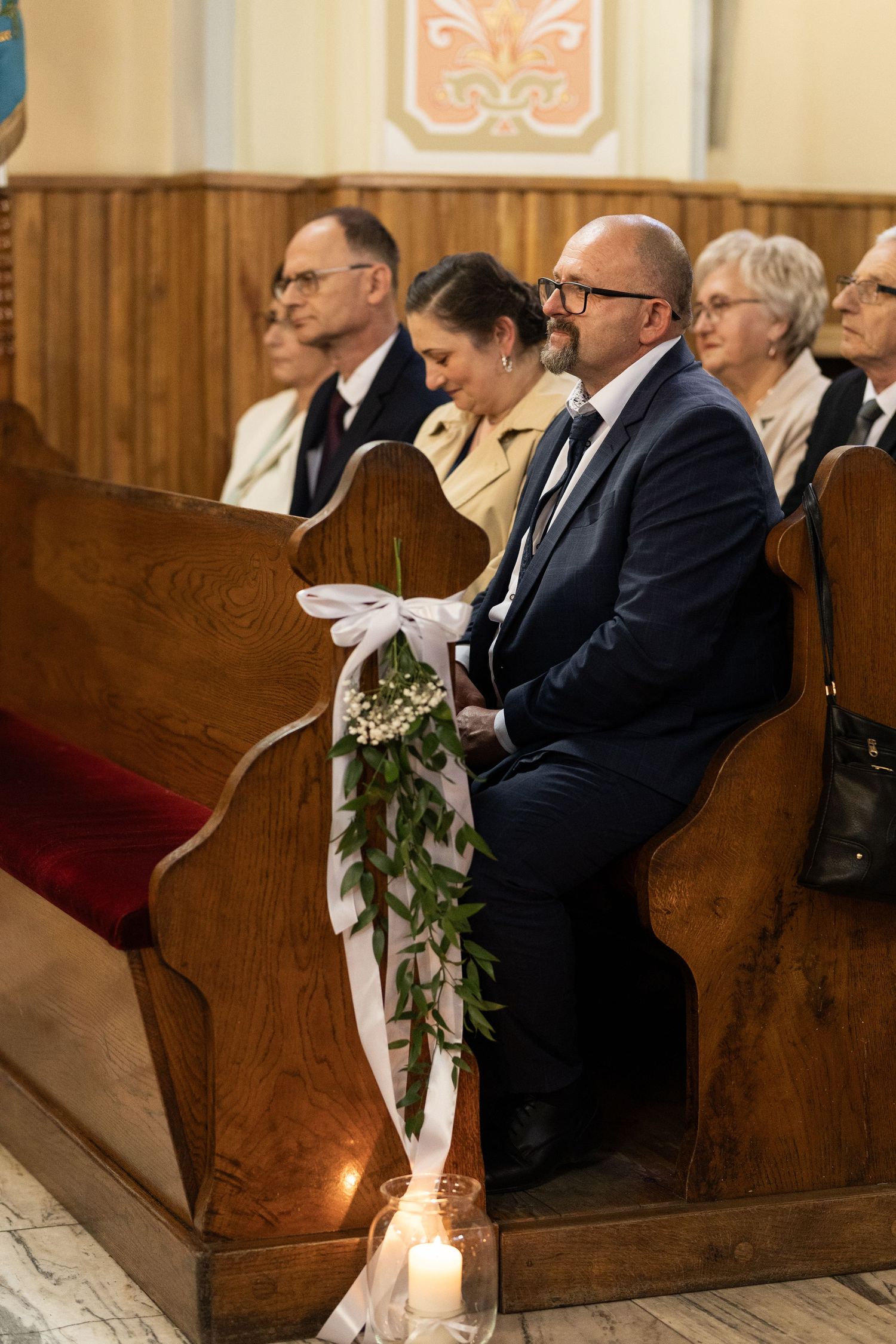People sitting in wooden church pews with candle and floral decorations during a special ceremony.