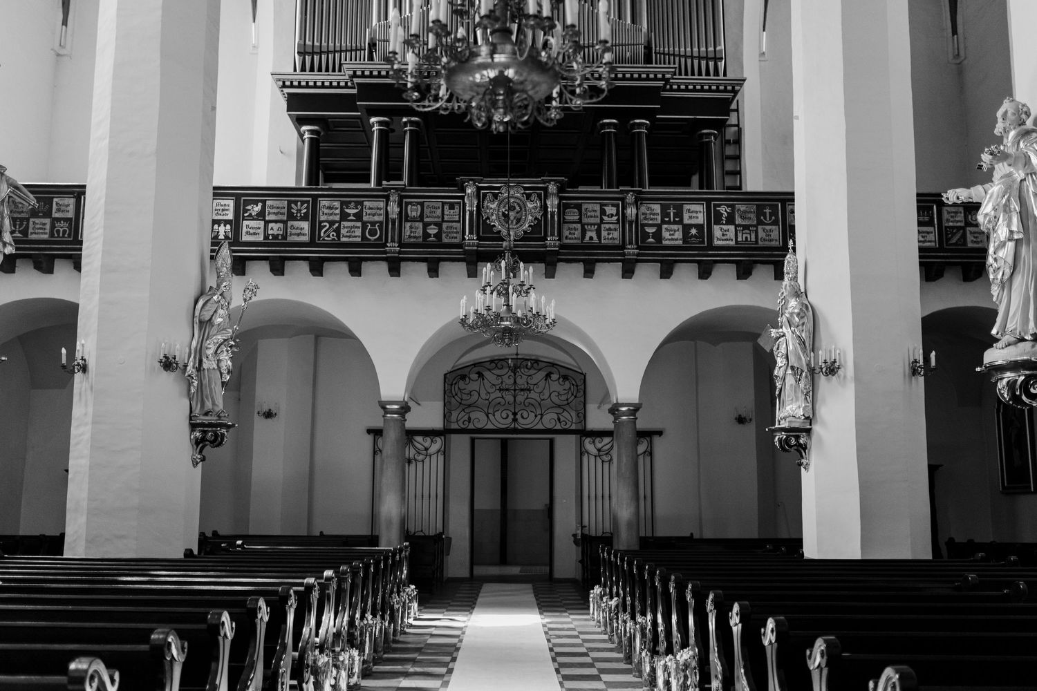 Interior of a historic church with ornate pipe organ, arched entrance, and rows of wooden pews in black and white.