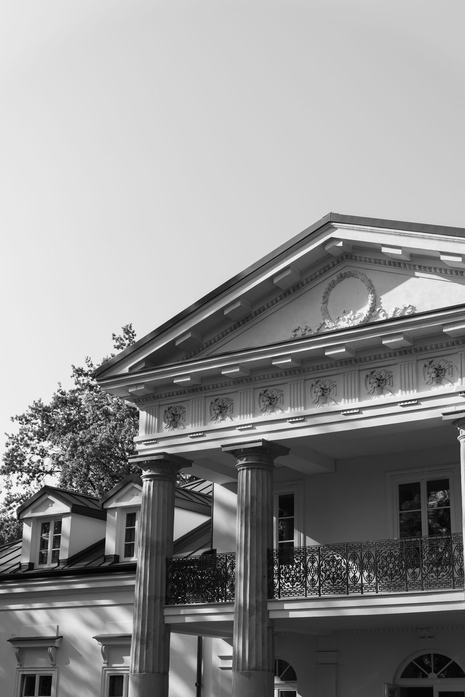 Architectural detail showing a white Greek Revival style building facade with columns and triangular pediment in sunlight.