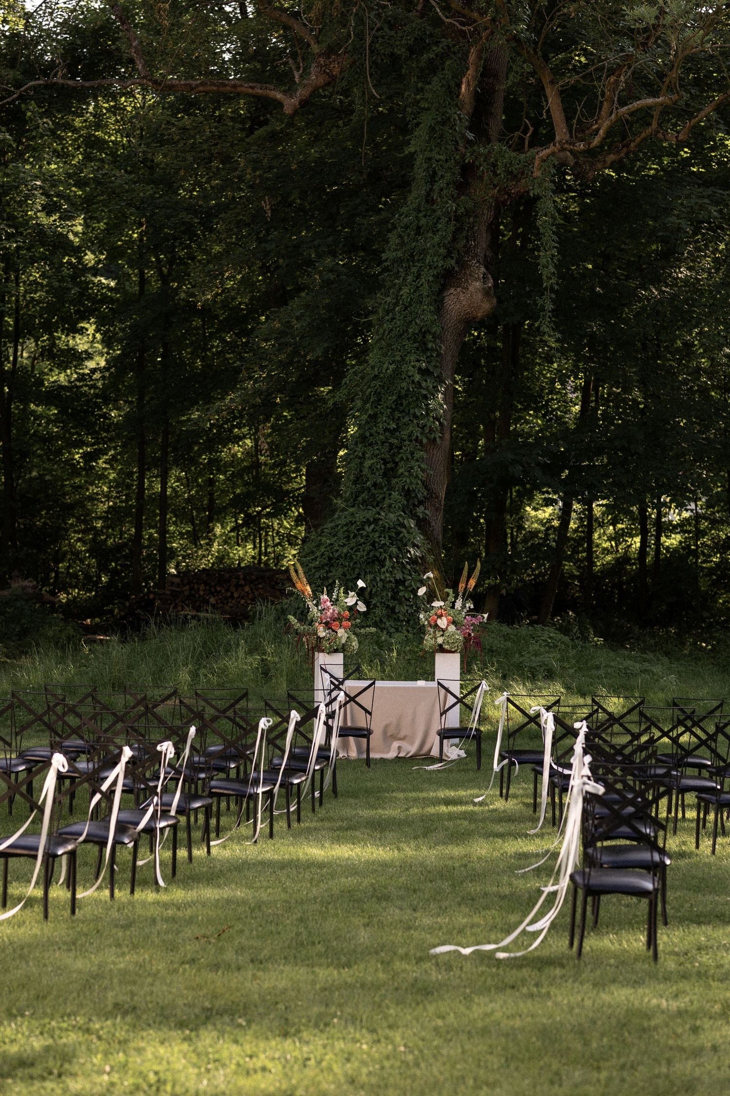 Black chairs arranged in rows on a grassy lawn for an outdoor wedding ceremony with white ribbon decorations.