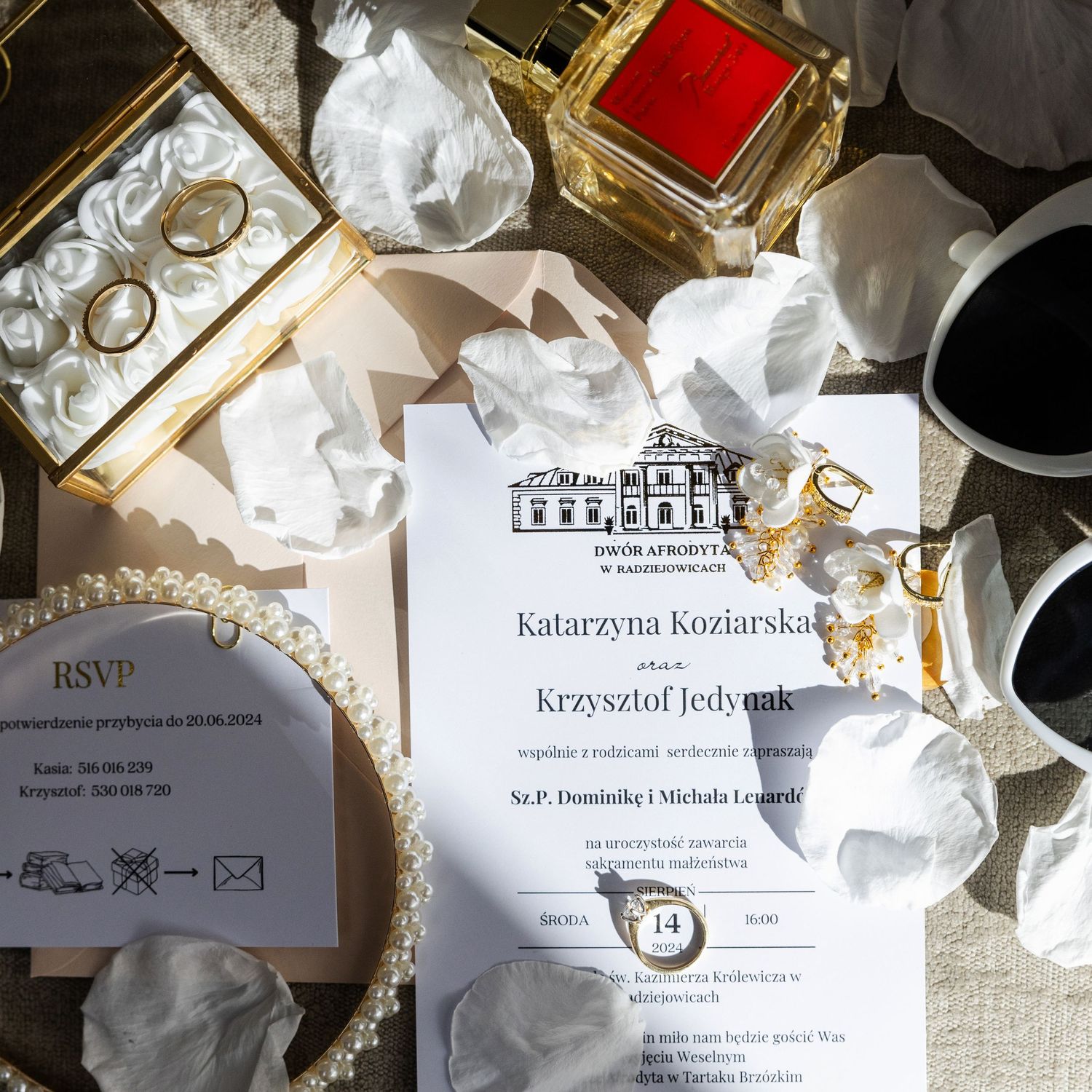 Wedding invitation with RSVP card surrounded by crumpled paper, gold decor items and rings on a table in natural light.