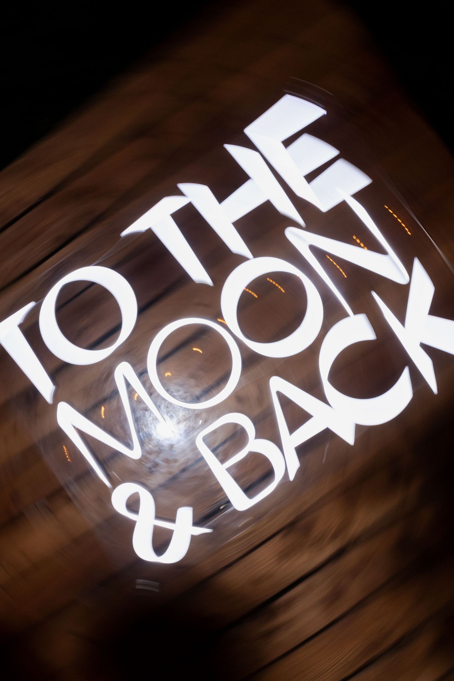 A white text logo saying 'TO THE MOON & BACK' displayed on a dark brown background with dramatic lighting.