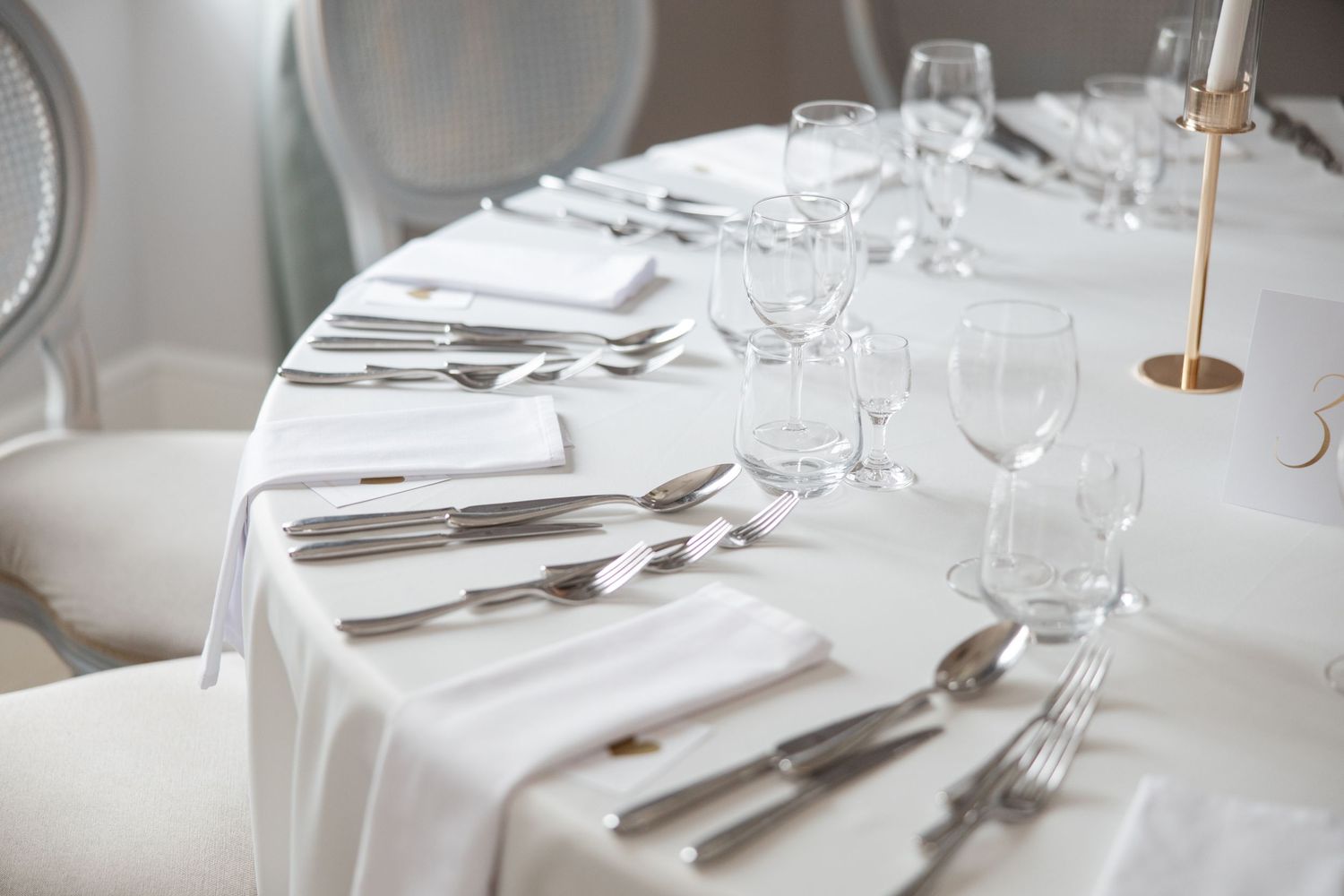 Elegant white table setting with silver cutlery, crystal glasses, and white napkins for a formal dining event.