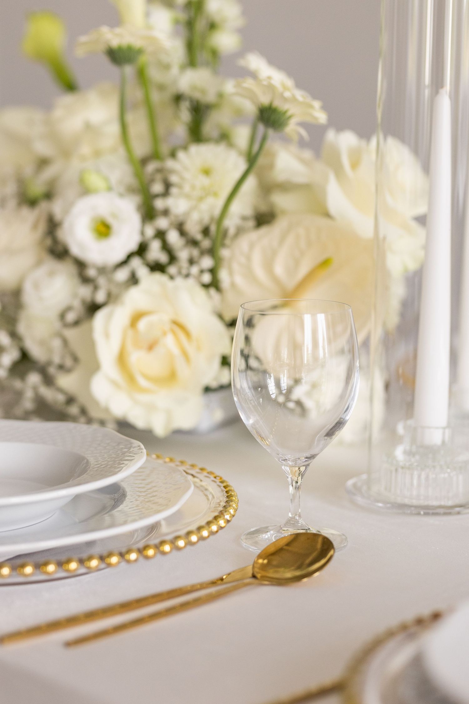 Elegant white table setting with cream roses, gold cutlery, beaded charger plates and crystal wine glasses.