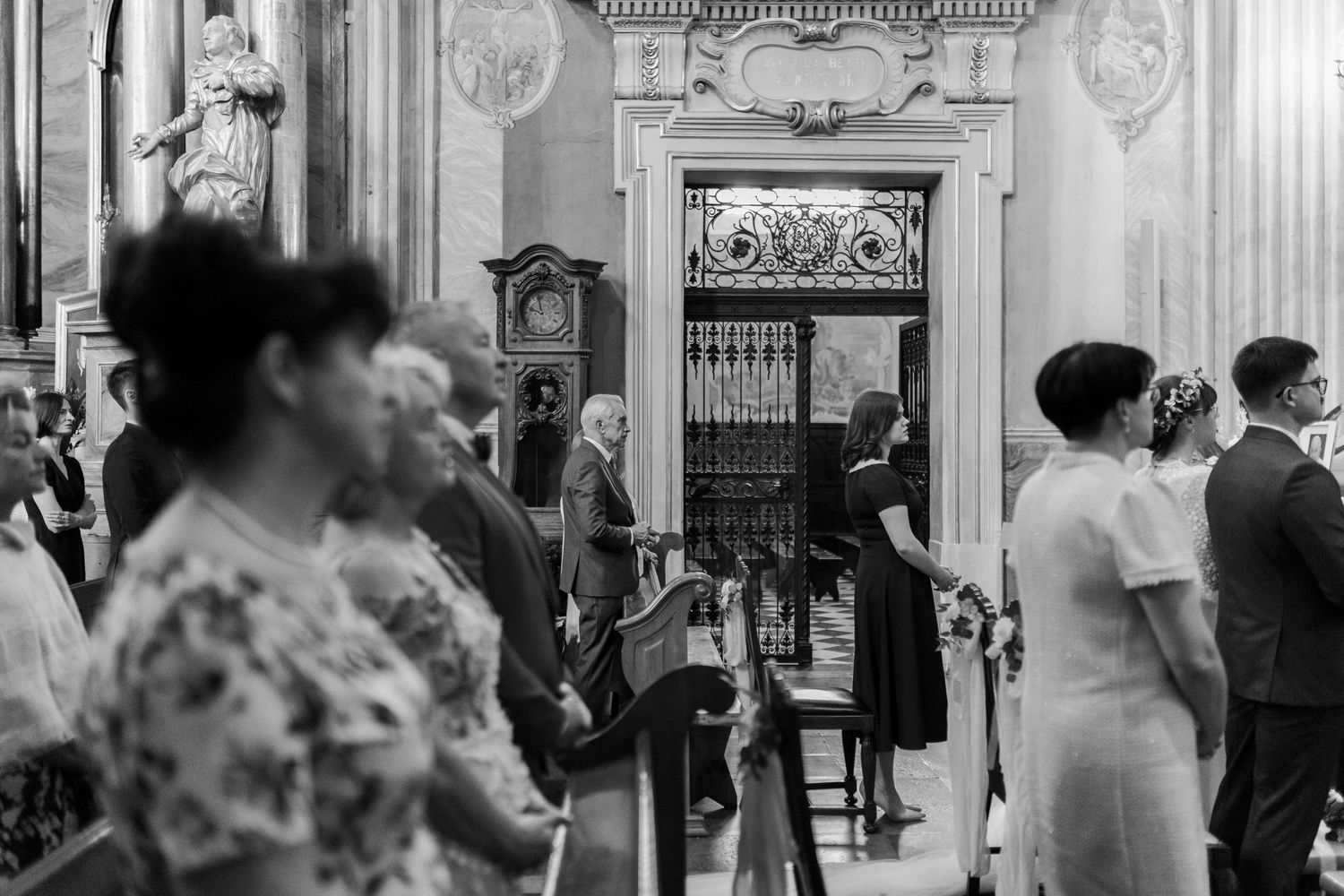 Vintage black and white photograph showing people gathered in an ornate interior space with decorative architecture.