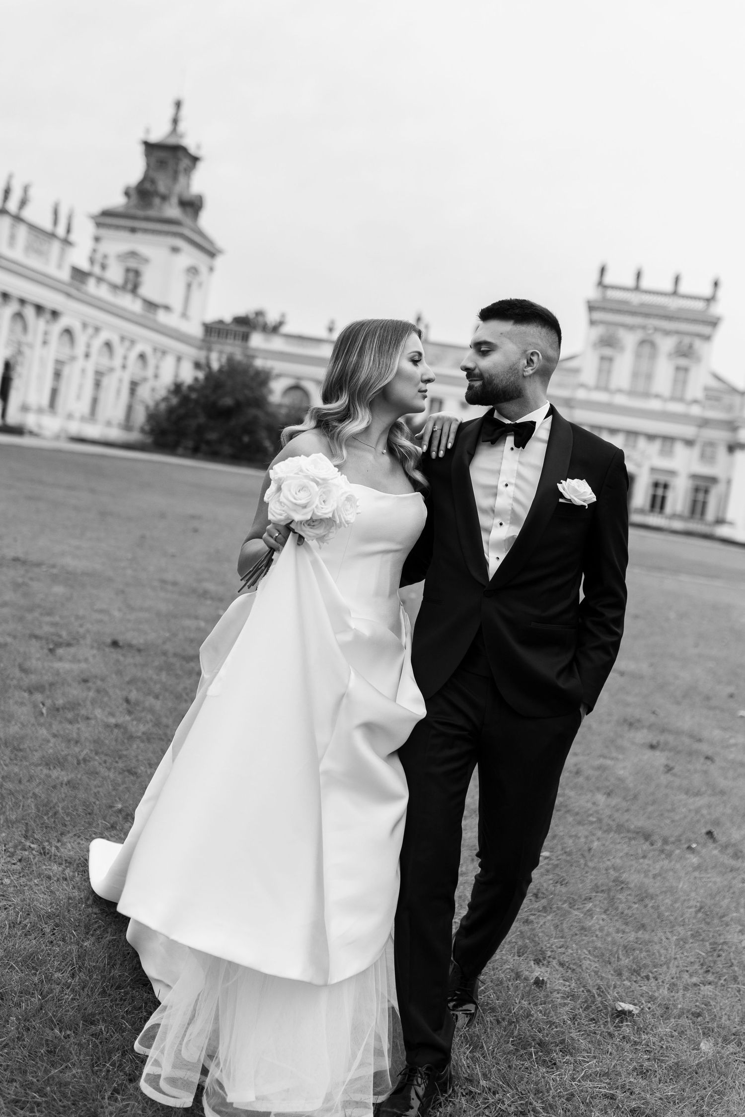 Black and white portrait of newlyweds in front of historic palace.
