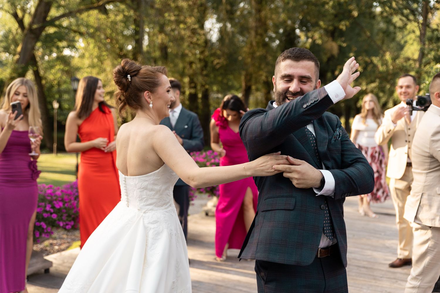 Newlyweds share their first dance outdoors on a stone patio surrounded by colorfully dressed wedding guests.