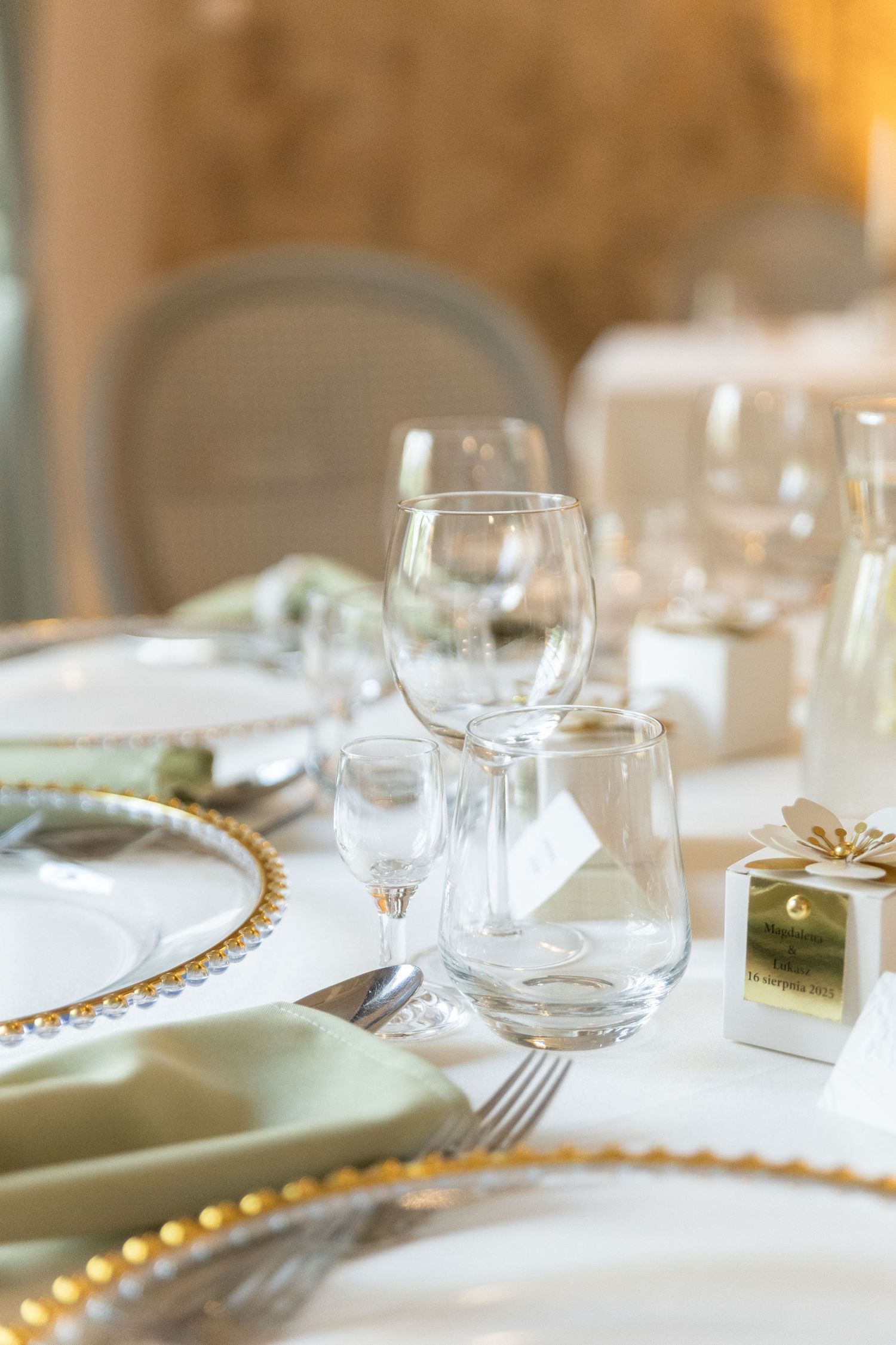 Elegant table setting with wine glasses, gold beaded charger plates, and white dinnerware in warm lighting.