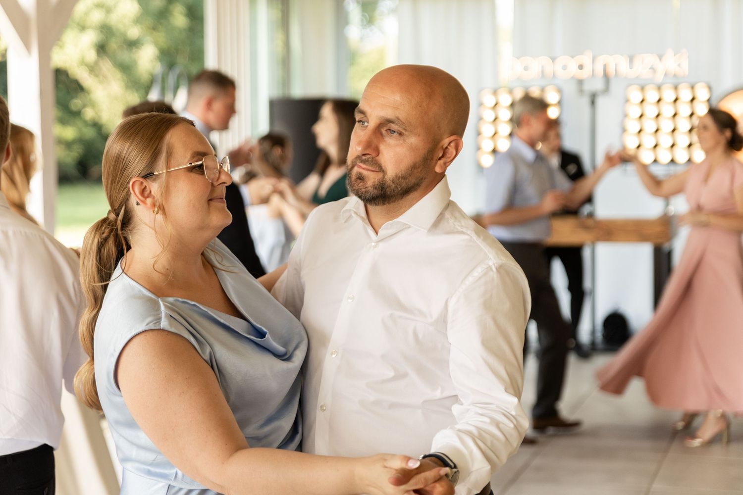 A couple dances together at a reception venue, with the person in blue laughing while their partner leads.