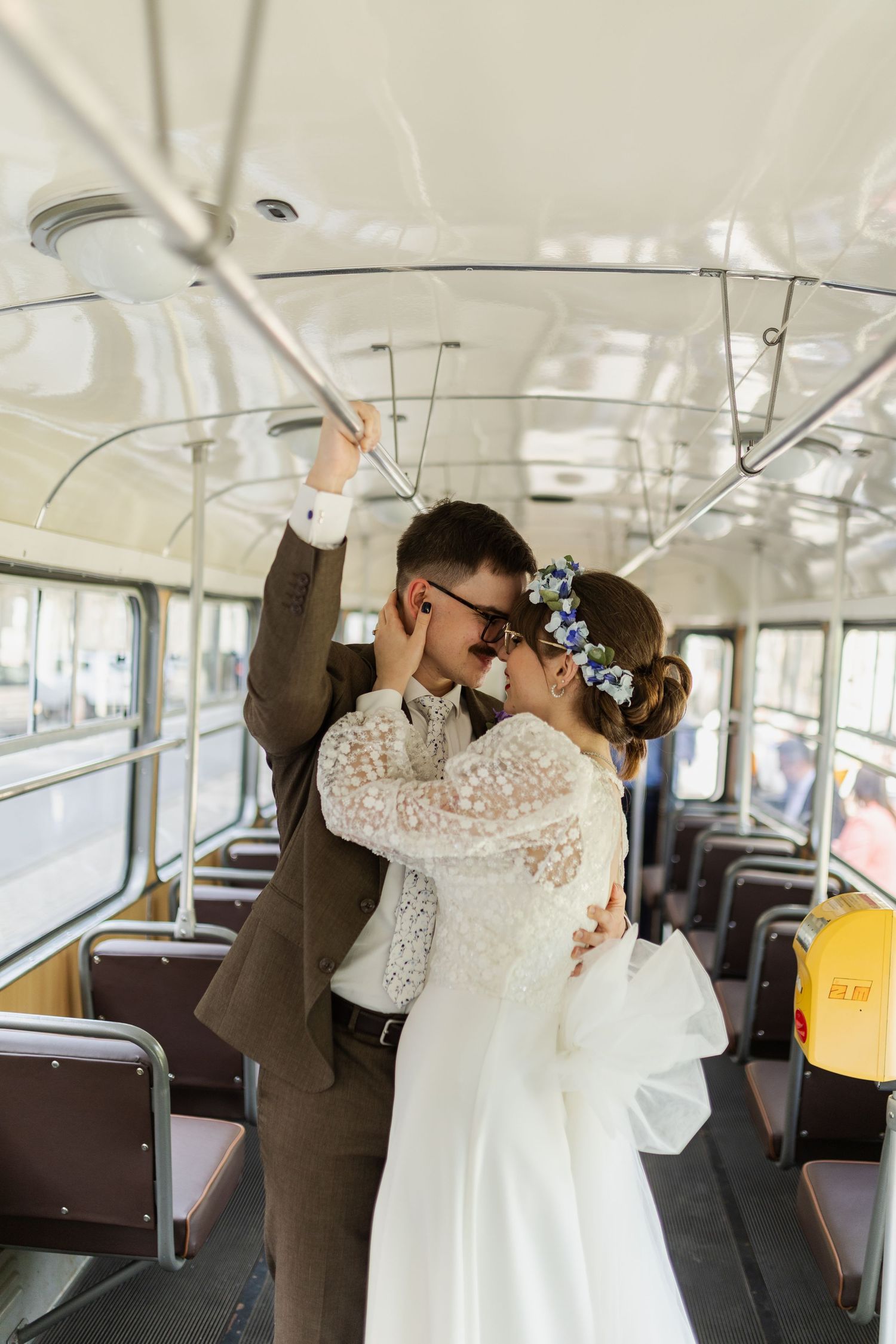 A romantic moment between newlyweds embracing inside a vintage bus, with the bride wearing a delicate lace dress and floral crown.