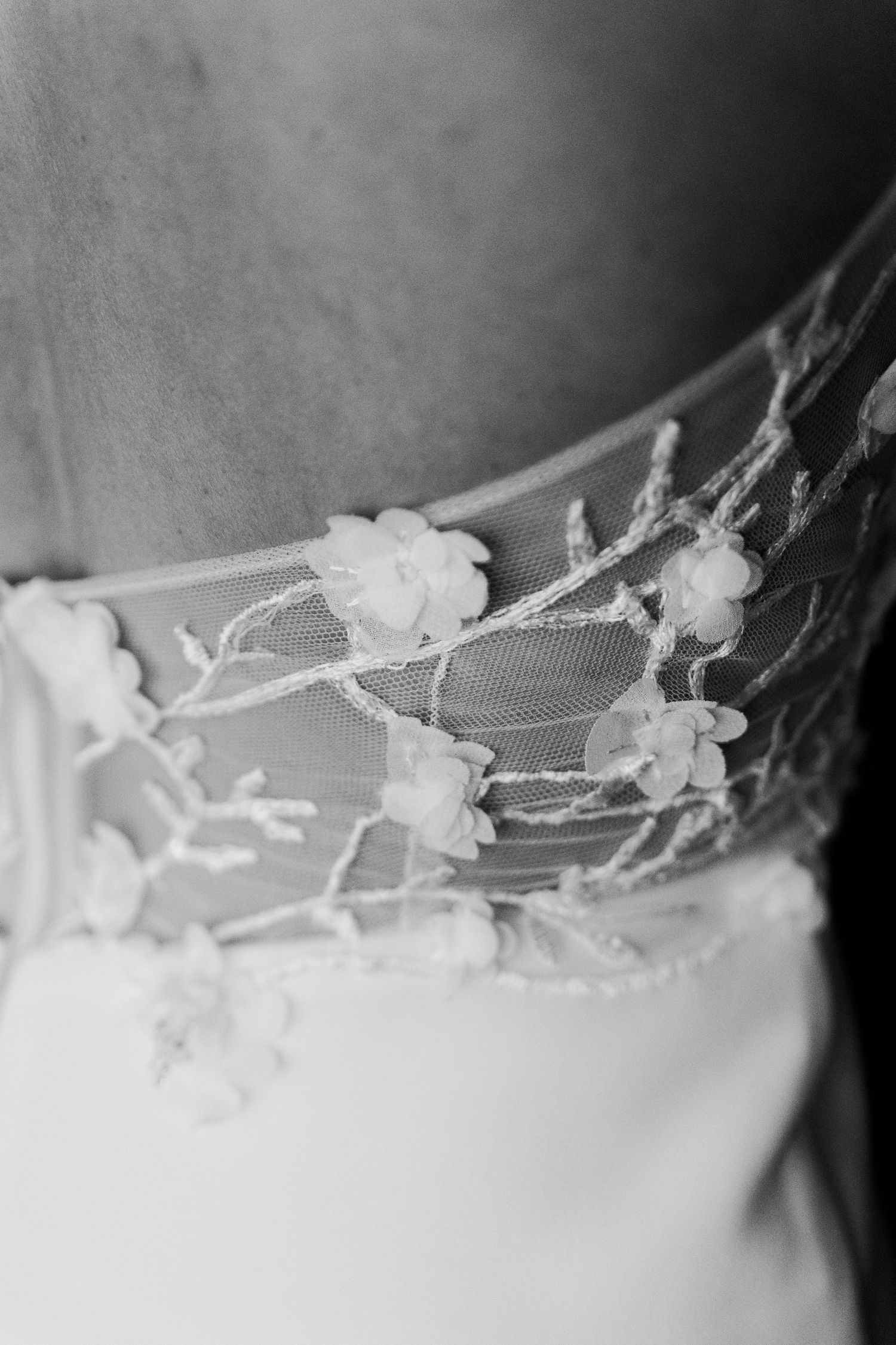 Close-up black and white detail of delicate floral lace and tulle embellishments on a wedding dress.
