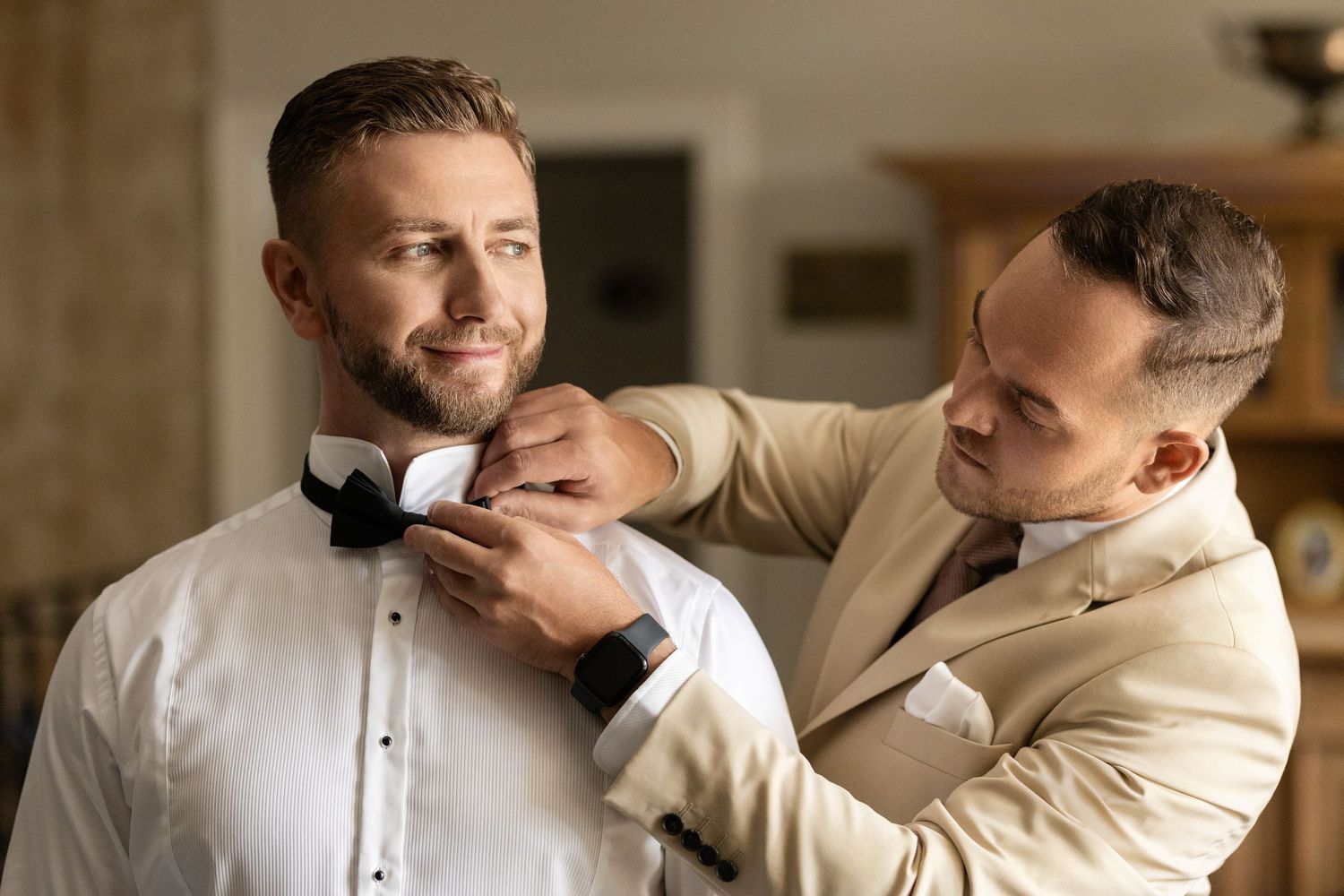 A wedding couple shares an intimate moment in a light-filled room while wearing formal attire.