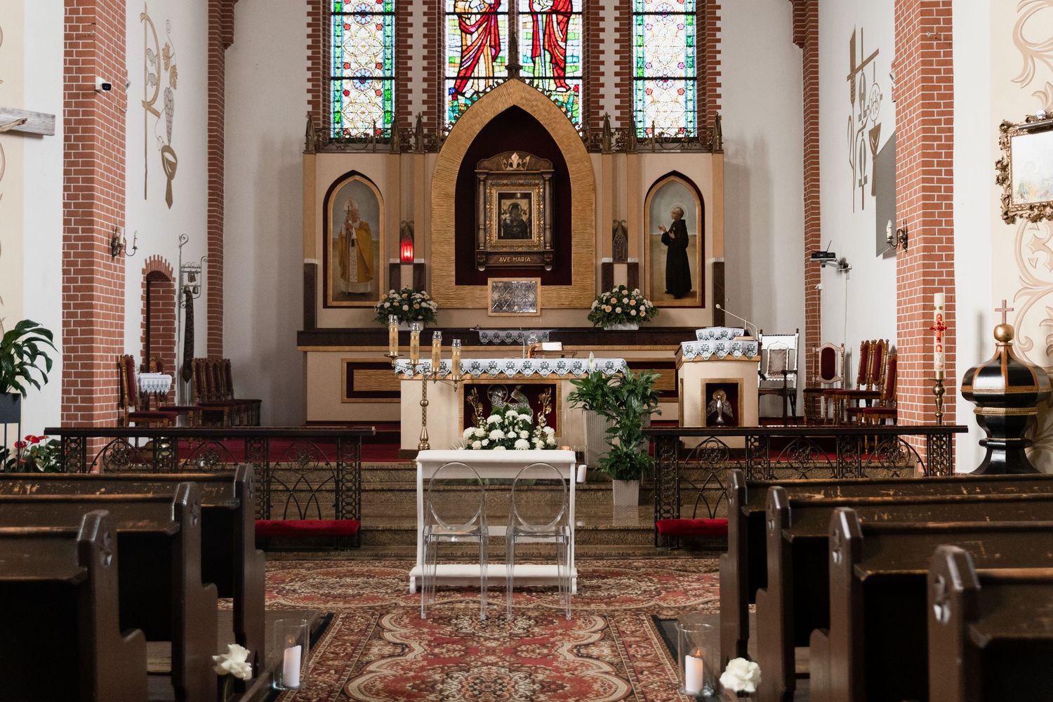 Interior view of a traditional Catholic church sanctuary with stained glass windows, altar, and red carpet aisle.