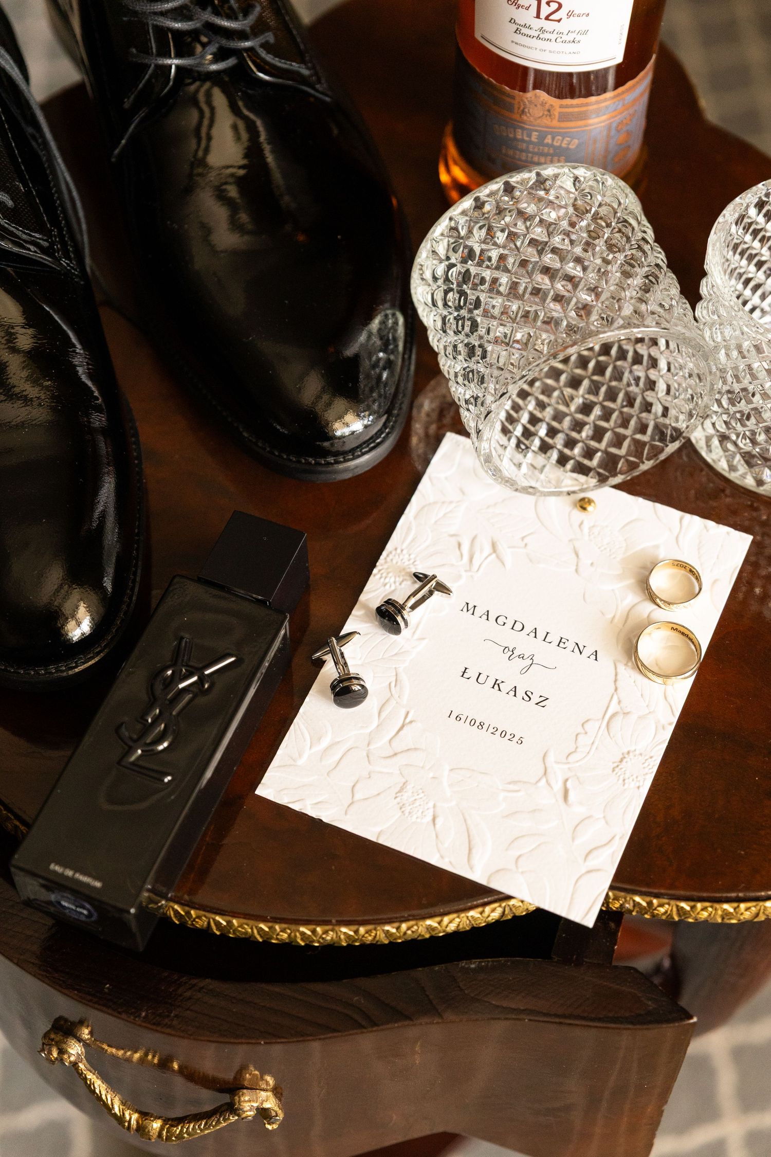 Close-up shots of wedding place cards and dress shoes arranged on dark wooden surface with gold trim details.