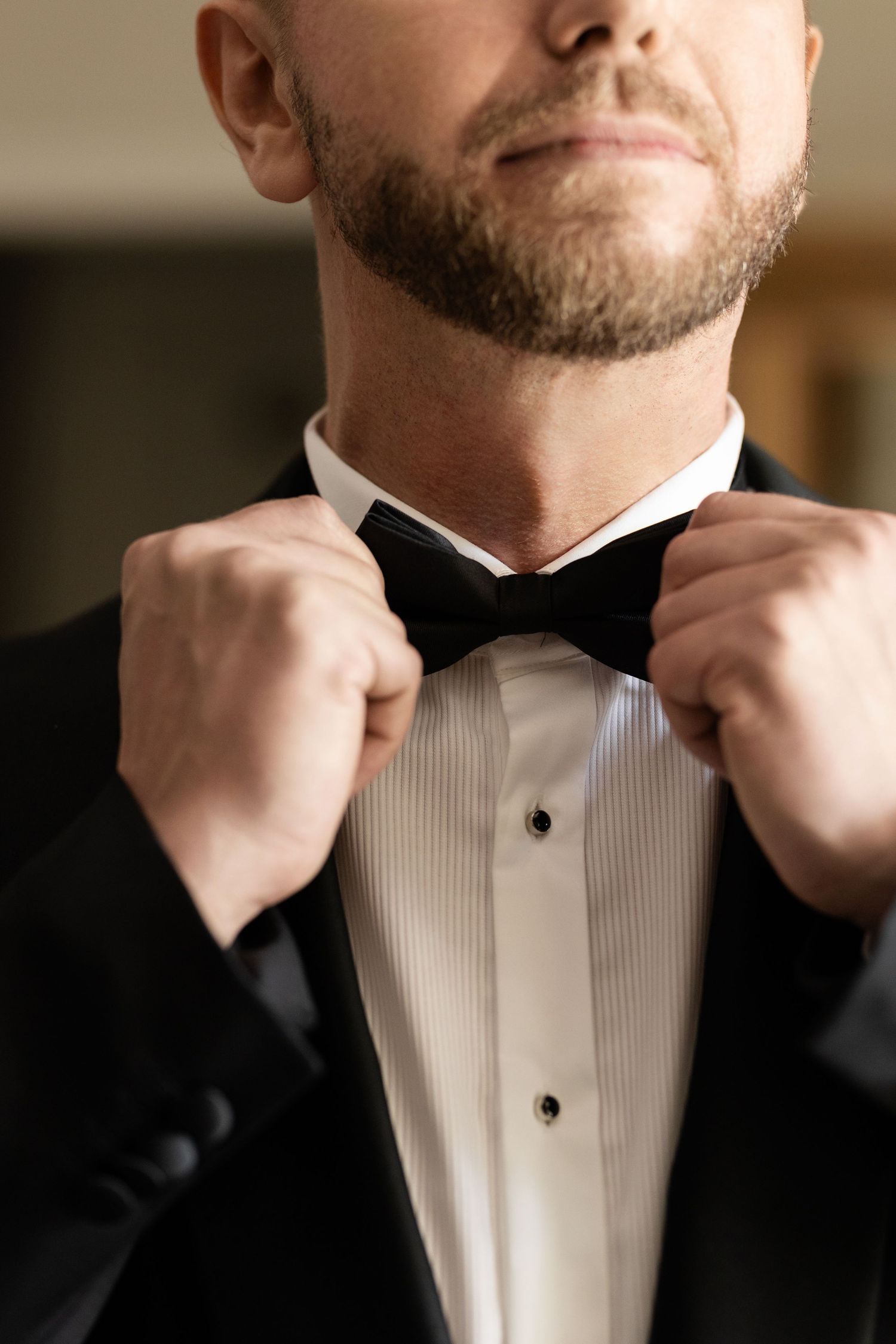Close-up sequence showing hands adjusting a black bow tie against a crisp white tuxedo shirt in formal attire.